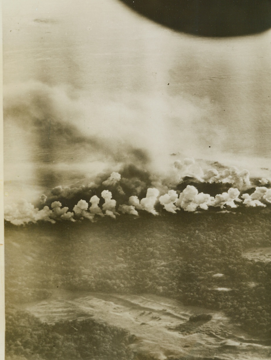 The Japs Don’t See the “Beauty” of it, 1/21/1944. New Britain – Almost perfectly aligned white blobs of smoke tell a success story of precision bombing by U.S. Army Fifth Air Force B-24’s and B-25’s who smack Cape Gloucester as the Marines move in.  The milky columns of smoke have a background of flame and darker smoke which shrouds the Pacific shore line.;