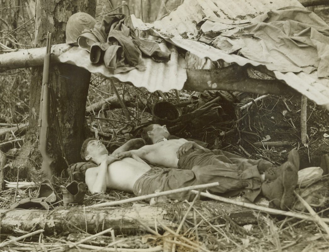 Babes In the Woods, 1/31/1944. Cape Gloucester – These two U.S. Marines were quick to take advantage of a lull in the fighting at the base of Hill 660, vital strongpoint in the Jap defense line near Cape Gloucester, to “hit the sack”.  Here, they sleep peacefully under a crude shelter to keep out the heavy rains, on the 18th day of the fighting for the hill, which eventually fell to the fighting U.S. Leathernecks. Credit line (ACME photo by Thomas L. Shafer for the War Picture Pool);