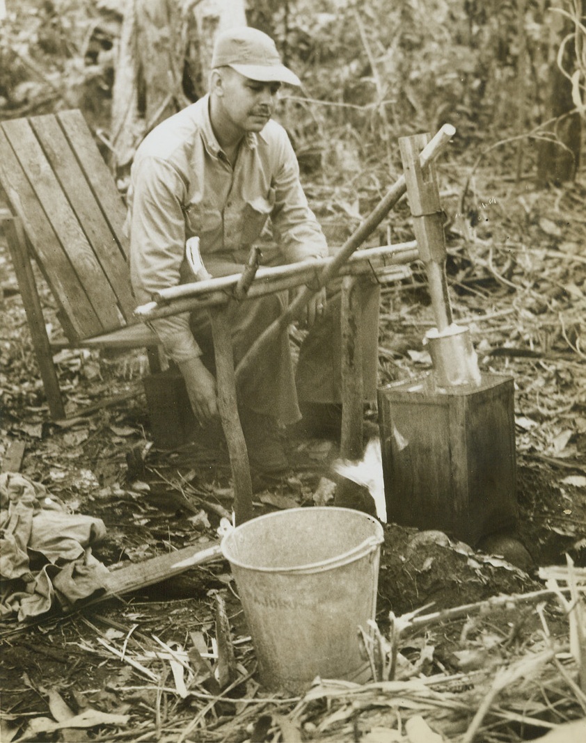 Wash Day in New Britain, 1/31/1944. New Britain – Major H.R. Kolp, USMC, of Akron, Ohio, does his washing in a homemade “washing machine”, made of a 10 gallon fruit can placed over a fire built in a pit.  An agitating plunger—a can at the end of a piece of wood—the clothes. Credit line (ACME photo by Thomas L. Shafer for the War Picture Pool;