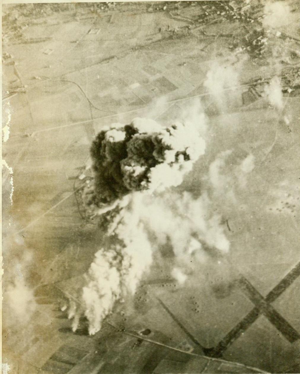 Nazi fuel goes up in smoke, 1/3/1944. A column of smoke, 4,000 feet high, rises from a German fuel storage dumb on the airfield at Chievres, France, after Martin B-26 Marauder medium bombers of the U.S. Army 8th Air Force had blasted it last Nov. 29. The concussion from exploding fuel was so great that the attacking bombers were bounced about in the air. The “X” (lower right), is the cross formed by the airfield’s runways. CREDIT LINE (U.S. Army official photo from ACME) 1-13-44;