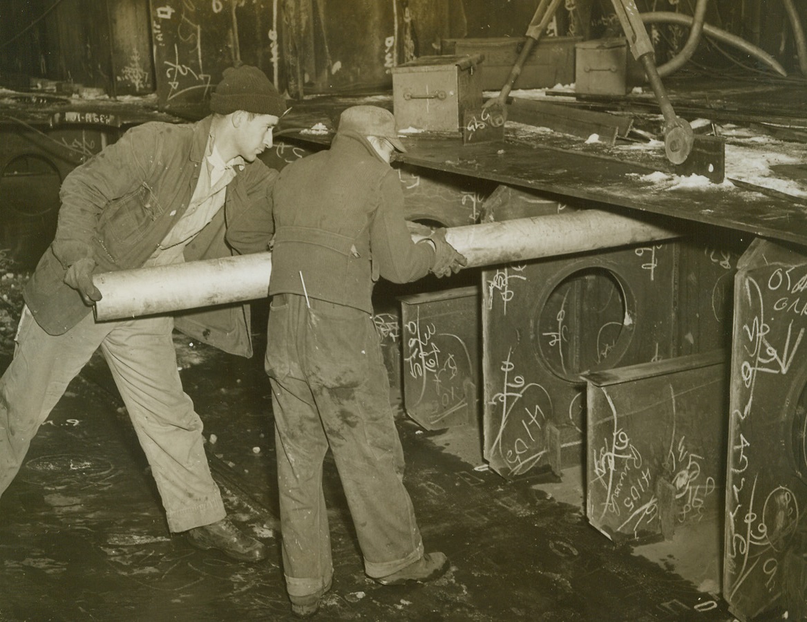 Flattop Under Construction, 1/21/1944. Newport News, VA. - Plumber H. H. McCracken (left) and his assistant, T. C. Ray, install an oil pipe peep in the bowels of one of the Navy’s new 45,000-ton Aircraft Carriers. This is the first photo ever released showing any work on the Navy’s giant flattops. Credit: Official U.S. Navy photo from ACME;