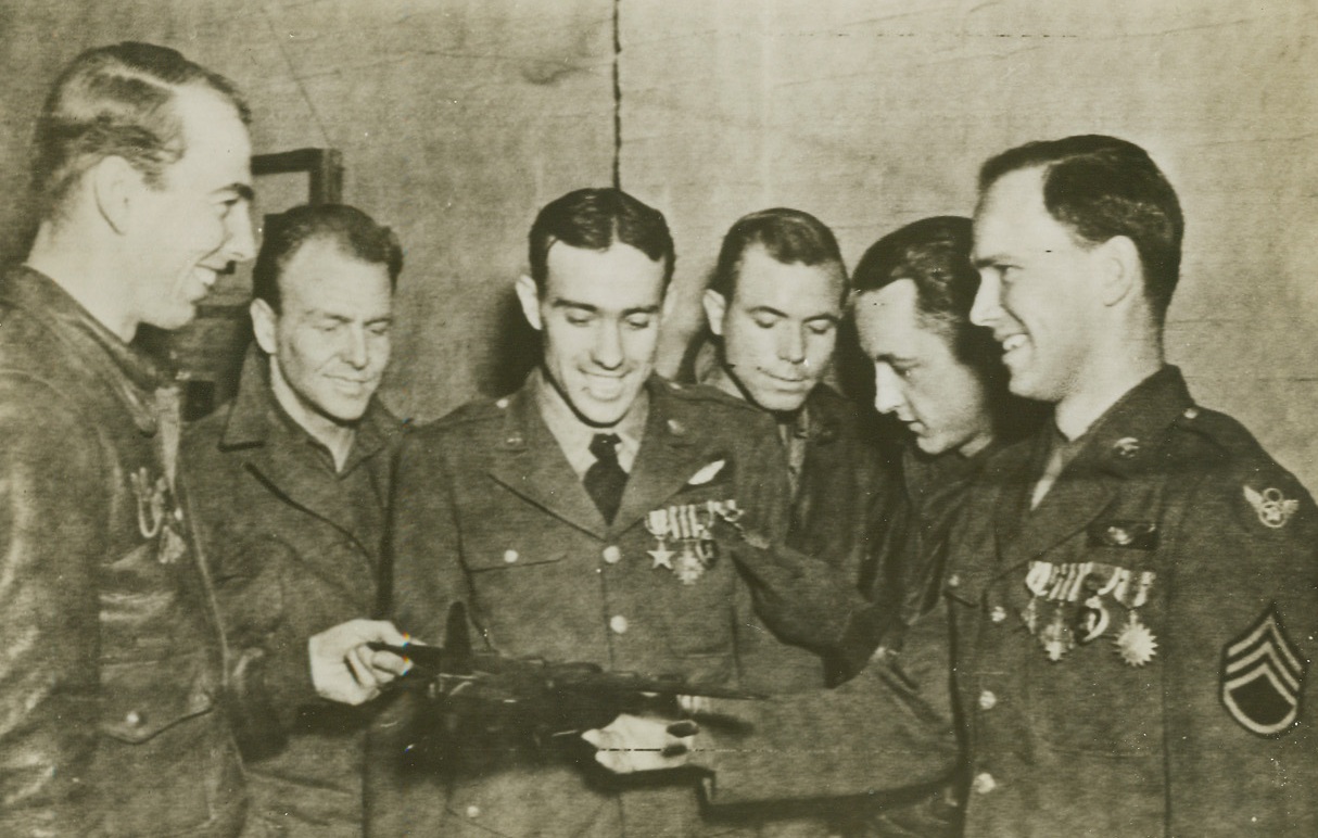 Seven in One Day, 1/31/1944. England – S/Sgt. Oliver R. Germann, 25, of Moran, Wyoming, extreme right, who received seven decorations in one day, the Silver Star, DFC with Oakleaf Cluster, Purple Heart, Airmedal with Three Oakleaf Clusters, holds a wooden model of a bomber given by S/Sgt. M. Hall, of Sanger, California, extreme left. Others watching the little ceremony are, left to right: S/Sgt. F.B. Mellums, of Springfield, Tennessee; S/Sgt. L.L. Ackerman, of Fox, Arkansas; T/Sgt. B.R. Smith, of Insull, Kentucky; S/Sgt. J.A. Crowder, of Luden, Tennessee, and S/Sgt. Oliver Germann. Credit: ACME;