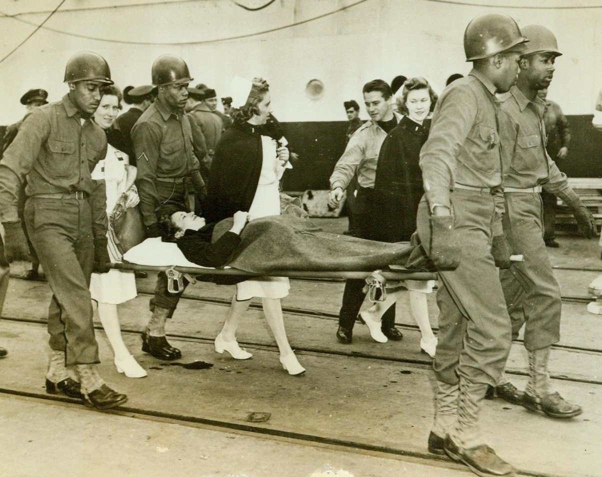 Army Nurse Comes Home, 1/8/1944. At an East Coast Port—Medical Corpsmen carry the stretcher on which Lt. Anna K. Smith came back to her native America. Smiling happily form her litter, the Army nurse was the first stretcher case to come off the U.S. Army hospital ship Acadia when it docked at an east coast port, bringing many casualties back from the battle zones. 1/8/44 (ACME);