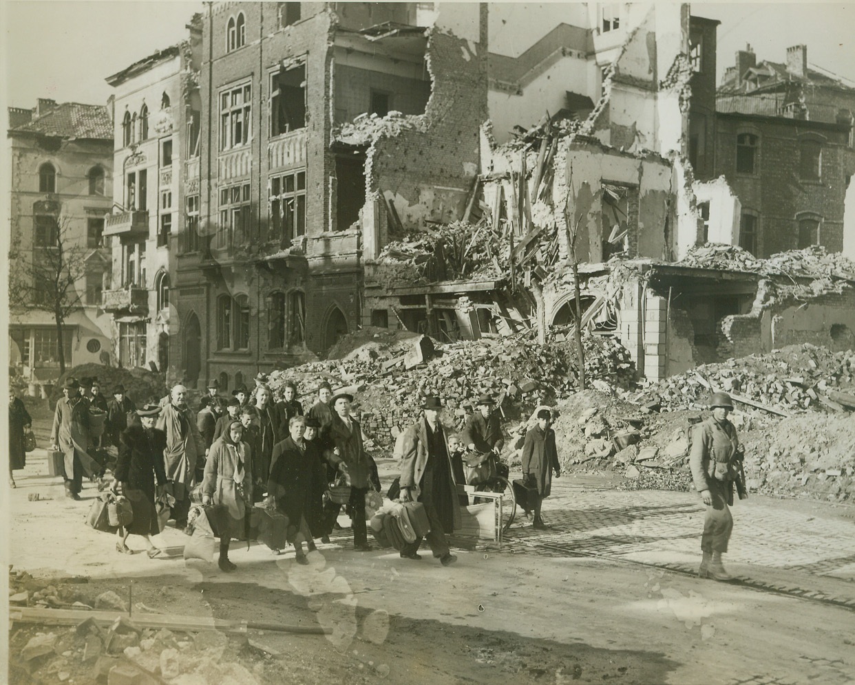 Leaving a Sinking Ship, 10/20/1944. Aachen, Germany – Carrying a minimum of baggage, German civilians leave their cellar hideouts in Aachen and head for safer areas, led by an American soldier. Supreme Allied Headquarters announced today that the last enemy resistance had been mopped-up, and the city is in the hands of the American First Army – the first great German city to fall to the Allies. Credit (ACME photo by Bert Brandt, War Pool Correspondent);