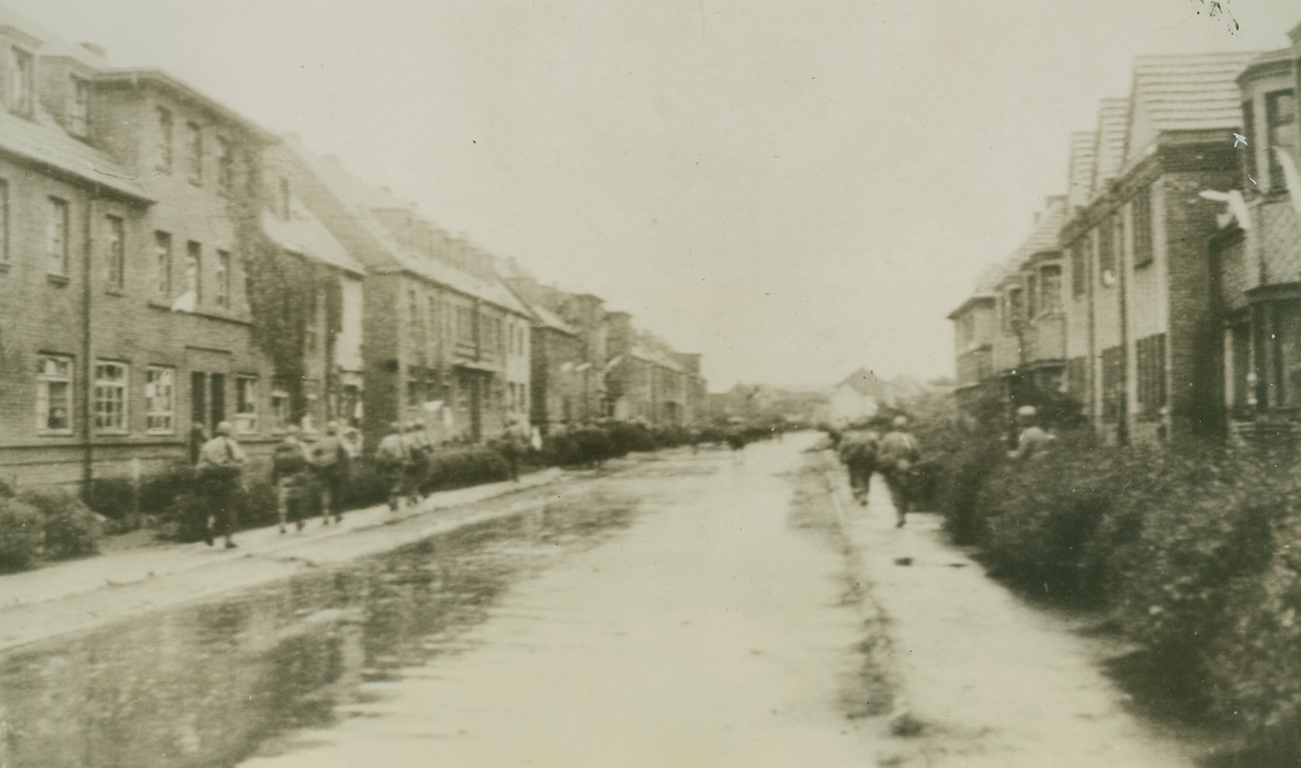 “LAUNDRY SALUTE”, 10/19/1944. GERMANY—Bits of sheets and other white cloth hang from houses on both sides of the street in this town beyond Kohlscheid, in token of surrender as U.S. Infantrymen advance through the rain in search of the enemy.Credit: Army Radiotelephoto from Acme;