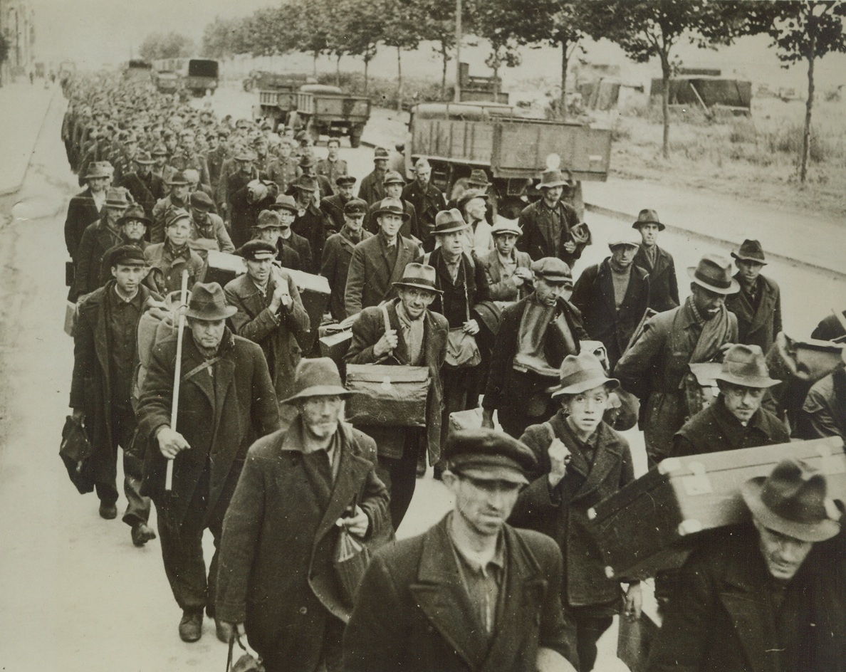 TAKE GERMAN PRISONERS—SOME IN CIVVIES, 10/19/1944. A crowd of German prisoners march to boats which will carry them to England. Those in civilian clothes have been rounded up after removing their battle outfits in an effort to avoid capture. Credit: British official photo from Acme;