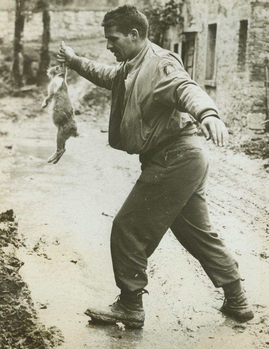 BUNNY DUCKS THE MUD, 10/19/1944. ITALY—Pfc. Lloyd F. Tegge, of Waukesha, Wis., carries his pet rabbit, “Rexine Gothic” across the ooze of a road in the Pietramala area. The prize bunny has been through the entire Gothic Line sector with its master, who is attached to the 5th Army. Credit: Army photo from Acme;