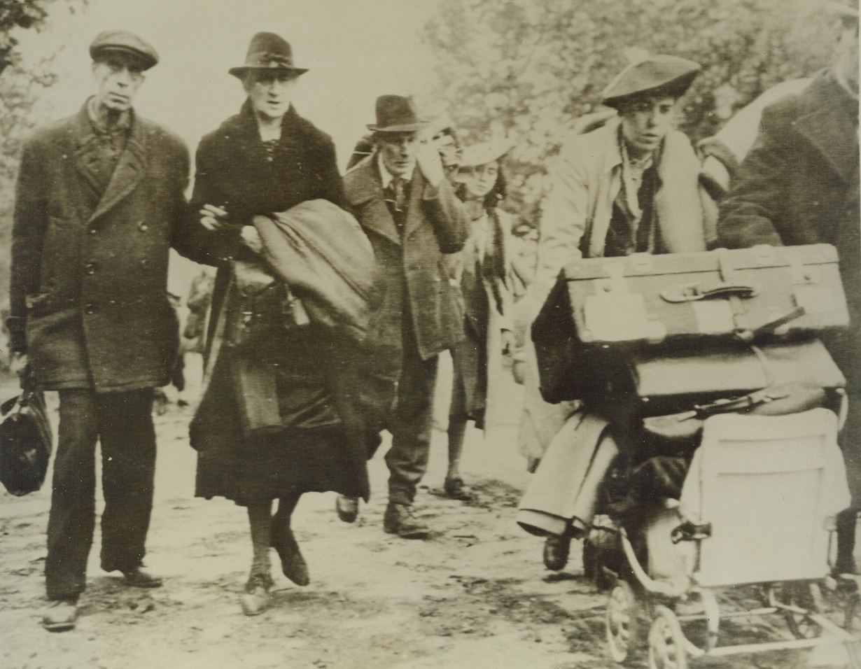 WAR WEARY GERMANS FLEE AACHEN, 10/17/1944. GERMANY—Civilian residents of Aachen leave the flaming city after their surrender to American forces. The refugees carry or cart their meager belongings as they march to safety. The dazed and worn expression on all tells the story of endless days of concentrated bombings. Credit: Army radiotelephoto from Acme;