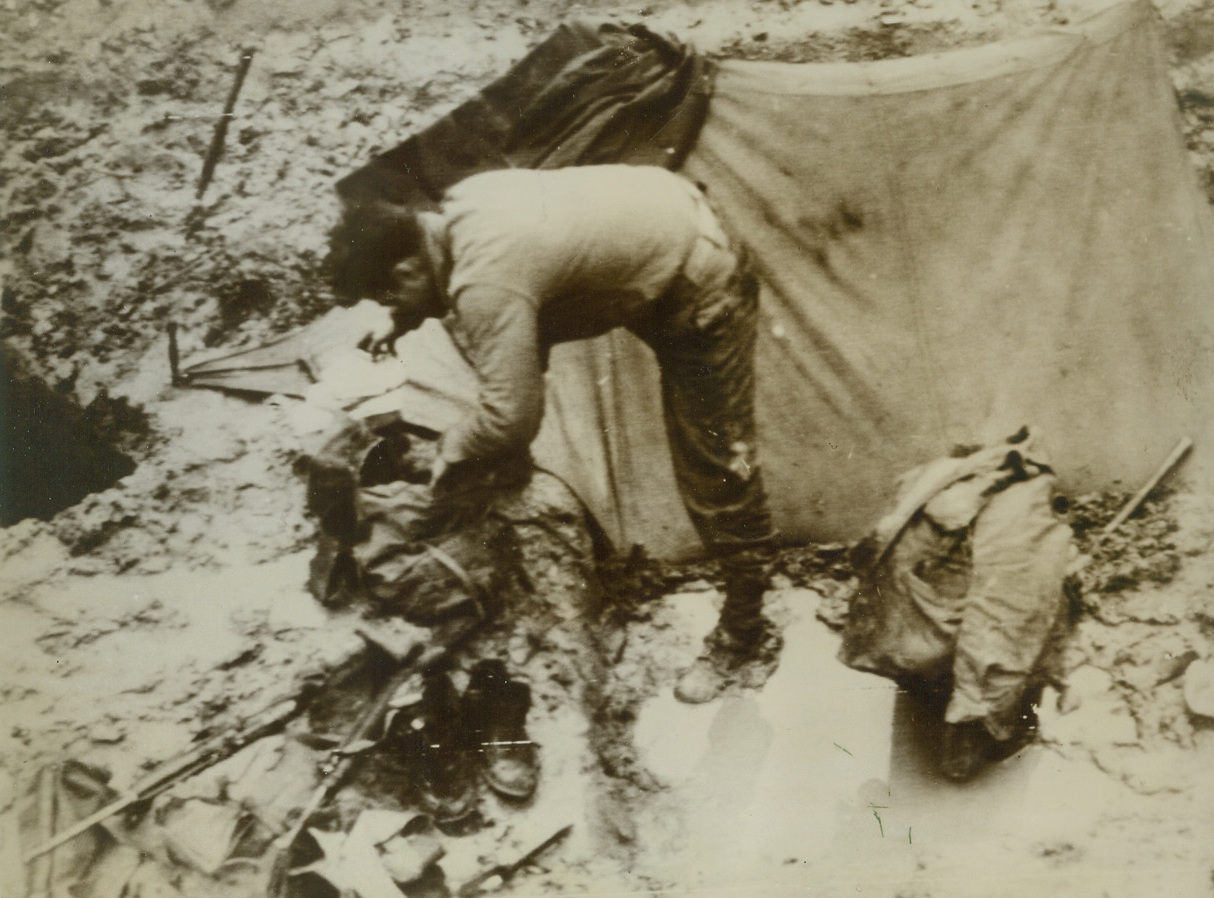 YANKS HIT RAINY SEASON, 10/12/1944. GERMANY—An American soldier tries to find some dry clothing, after being rained out of his bivouac camp in a German tank trap. Rain and mud have been hampering Allied advance, particularly in the Luxembourg Sector. Credit: Army radiotelephoto from Acme;