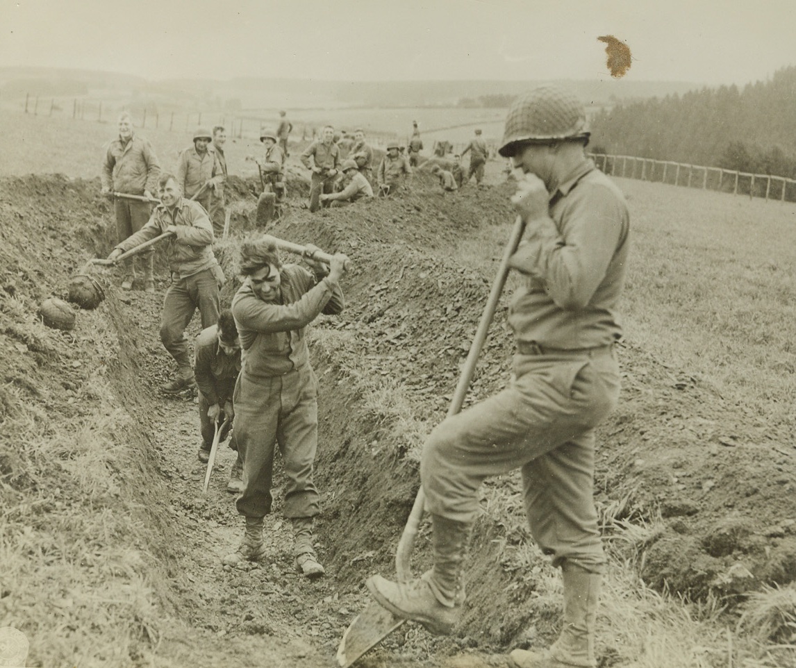 YANKS DIG IN—AGAIN, 10/19/1944. BELGIUM—Swinging shovels and picks with…will, U.S. Infantrymen dig in along the…line of trenches used during Word War…to protect themselves from enemy action. Credit: U.S. Signal Corps photo…;