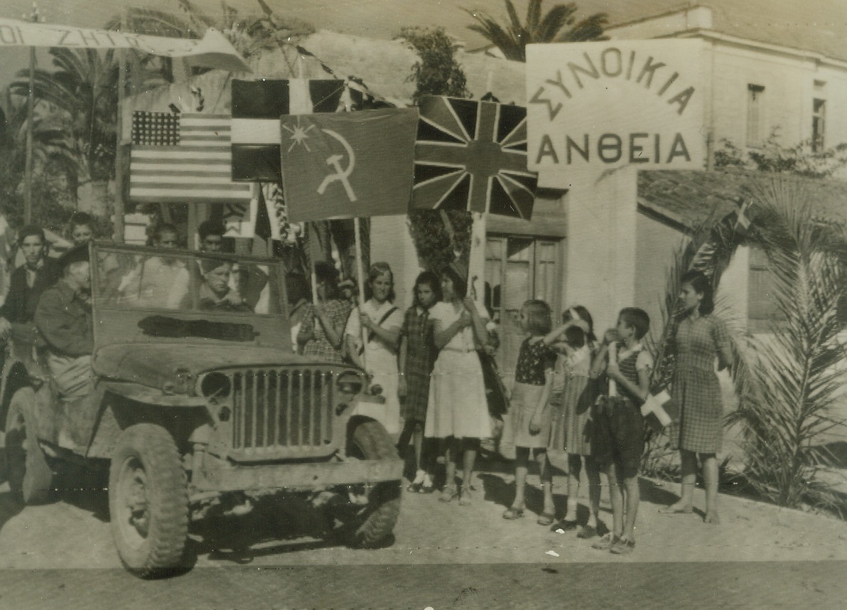 Greek Children Welcome RAF, 10/9/1944. PATRAS, GREECE -- As members of the RAF ride into liberated Patras in armored cars, Greek children into the streets, carrying banners of welcome and flags of the Allied nations. The sign is a welcome in Greek. Credit (ACME Radiophoto);