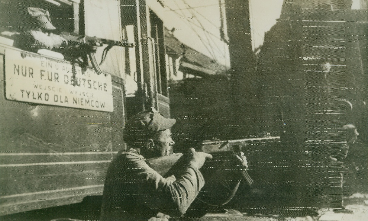 Polish Patriots Blast Nazis in Praga area, 10/1/1944. PRAGA, POLAND – One Polish tommy-gunner takes aim at German soldiers in Praga from the ground, while the other leans out the window of a trolley, which ironically bears a sign saying “For Germans Only.” Meanwhile, in nearby Warsaw, the situation is reported “critical,” and a German communiqué stated that more of the trapped troops were smashed in Warsaw, while others surrendered unconditionally. Praga is a suburb of Warsaw.Credit (Acme Radiophoto);