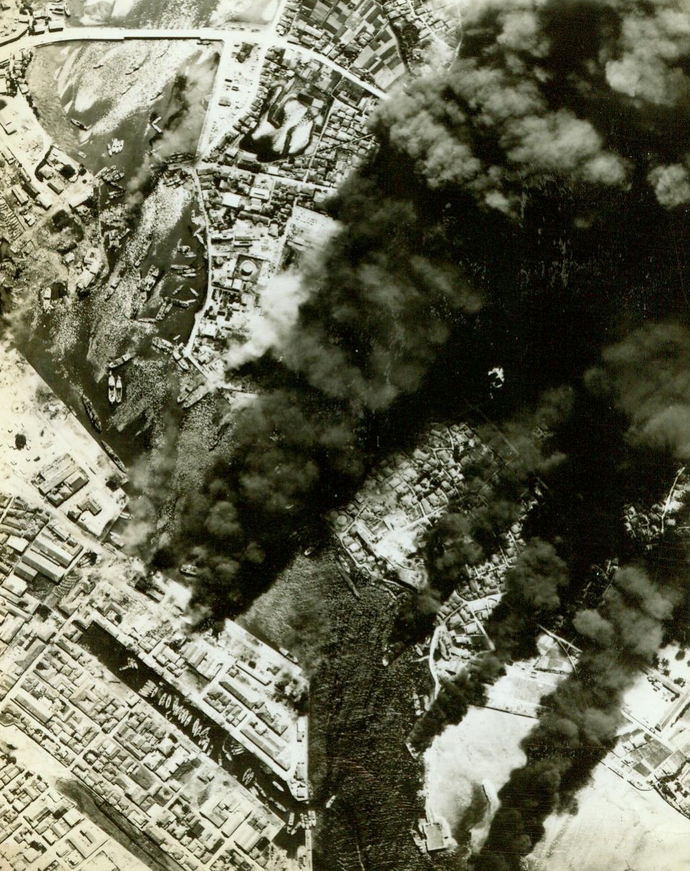 Ryukyu Industrial City Blasted, 10/18/1944. Naha City, Ryukyu Islands – Planes from Admiral Nimitz’s Pacific Fleet Strike devastating blows at Jap base in the industrial area of Naha City on Okinawa Island in the Ryukyu chain south of Japan. Burning warehouses and ships prove accuracy of Navy bombers;