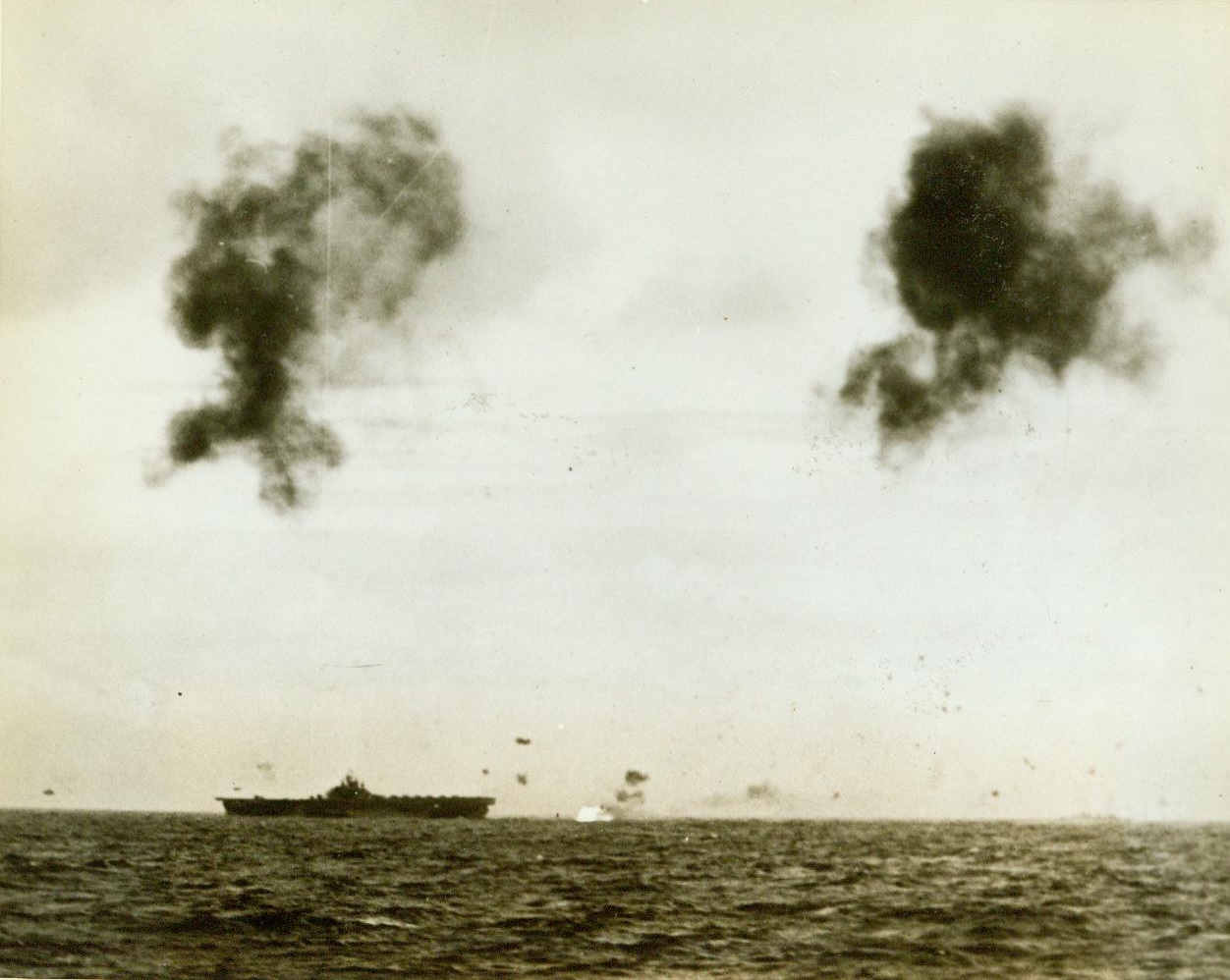 U.S. Carriers Throw Off Jap Attackers, 10/18/1944. Formosa – In a cloud of spray and flame, an enemy plane disappears just aft of an Essex class carrier. Another flier of the rising sun swoops over the carriers bow as anti-aircraft bursts pepper the sky. This is one of the first pictures of the fierce sea engagement off Formosa 10/18/44 Credit line (ACME);
