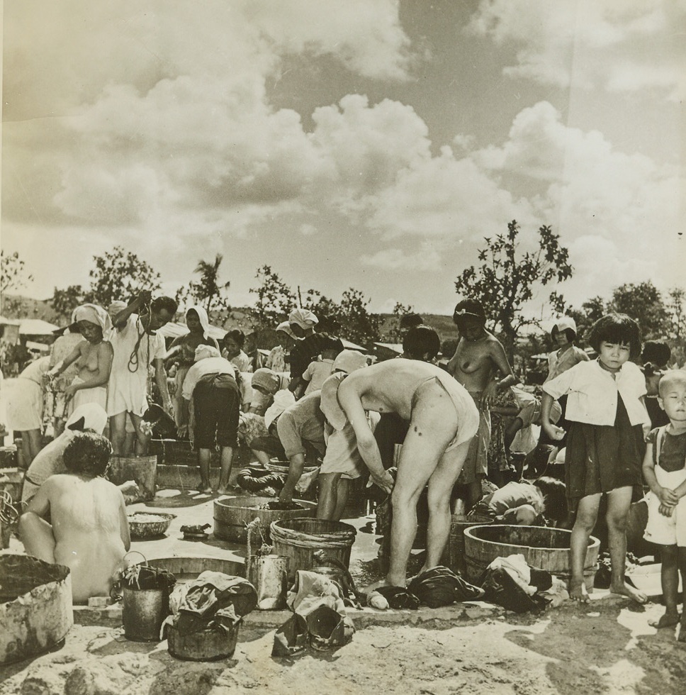 Civilian Life on Saipan, 10/27/1944. Saipan, Marianas  -- taught the value of cleanliness by US forces of occupation, Japanese civilians, Koreans, Kanakas, and Chamorro natives of Saipan bathe themselves at the community bath, using water handed to them by the bucketful.  Under Jap rule, these people lived under conditions of filth and starvation, and are just beginning to learn habits of health and sanitation, taught them by the American soldiers.Credit (ACME) (WP);