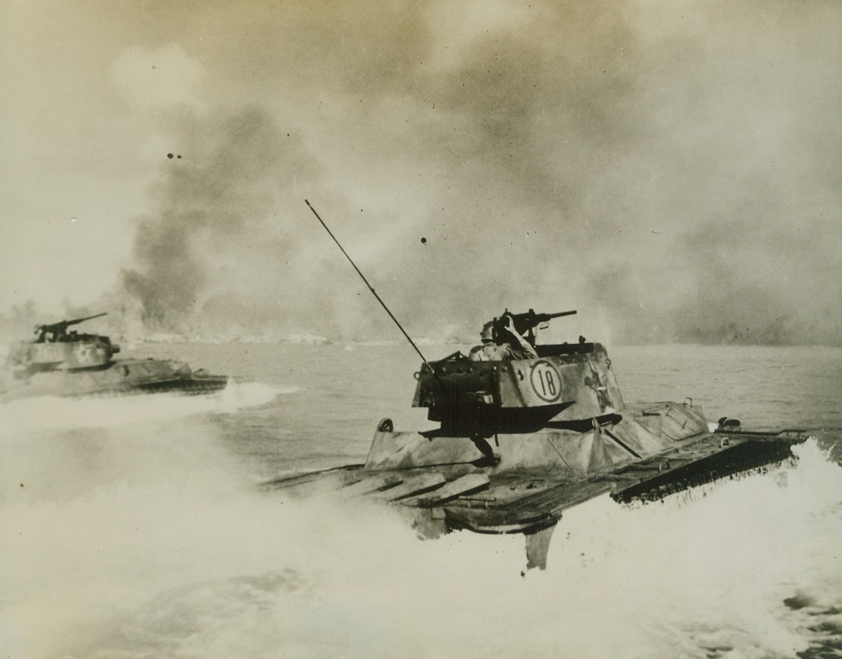 “Water Buffaloes” Head for Action, 10/1/1944. An gaur Is., Palau – Creating a backwash of foam and spray, tanks of a Marine Corps amphibious unit steam for the beach at An gaur, with machine guns and cannon ready for action in the initial assault upon the Jap stronghold.  Note in the background smoke and flames from burning beach installations, hit by the preinvasion bombardment. Credit (Official US Coast Guard photo from ACME);