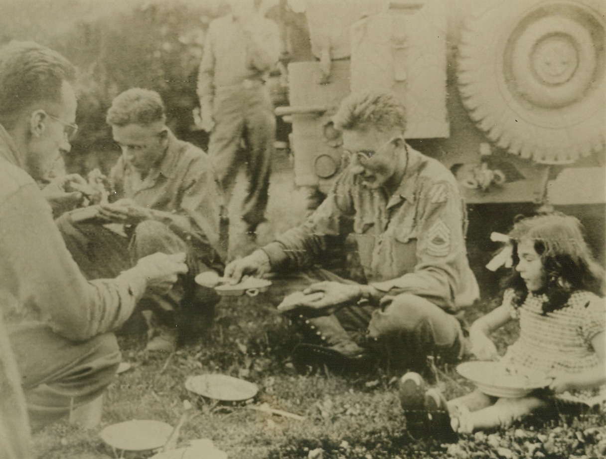 THE TOT WHO CAME TO DINNER, 10/2/1944. SOMEWHERE IN FRANCE – Sitting beside her new Yank friends, a tiny French girl shares pot luck with boys of the Third division as they squat for mess somewhere in France.Credit: Signal Corps Radio telephoto from Acme;