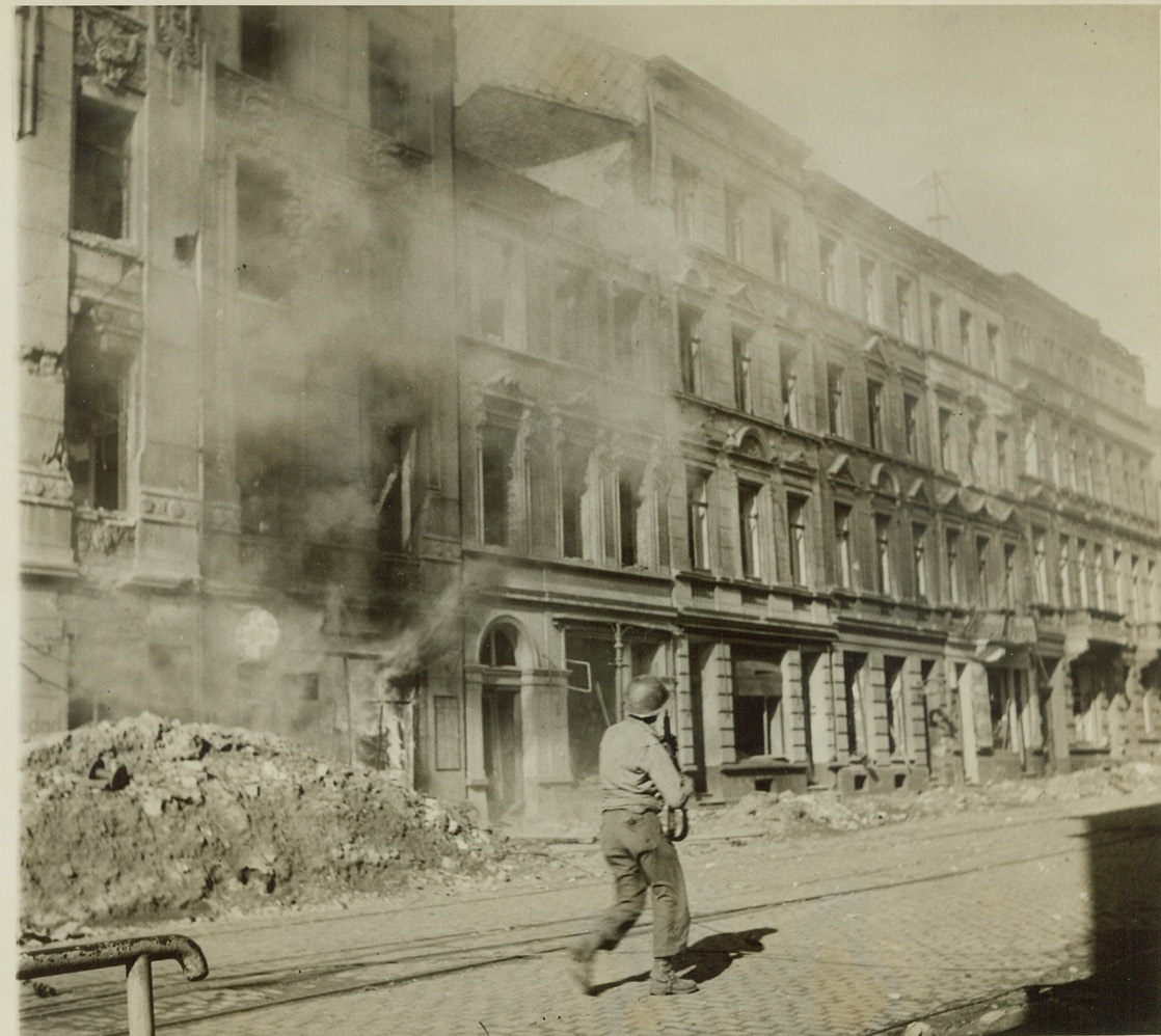 Shooting his way through Aachen, 10/20/1944. AACHEN, GERMANY – Moving up a street in Aachen, past buildings still smoking from exchanges of shots, this American infantryman keeps his gun cocked and eyes open for German snipers, as he leads an advance during the fierce street fighting final enemy resistance ended today, and American forces are now in full possession of the German town, key to the Rhine. Credit (Acme Photo by Bert Brandt, War Pool Correspondent);