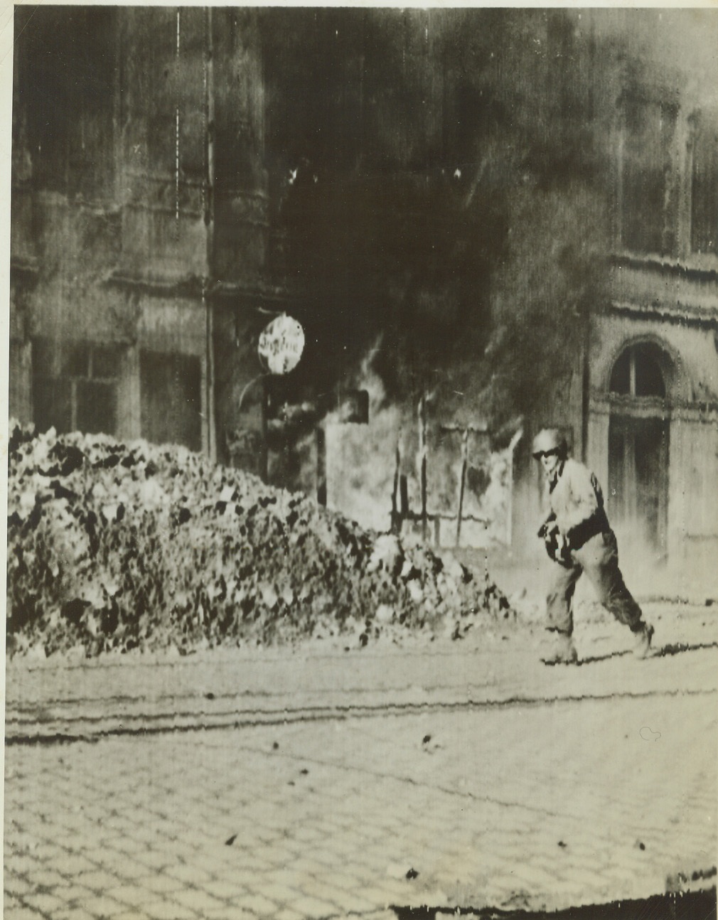 Inching Ahead in Aachen, 10/16/1944. AACHEN, GERMANY – Running past a blazing building, an American Infantryman advances through the streets of embattled Aachen. Credit: (Army Radiotelephoto from ACME);