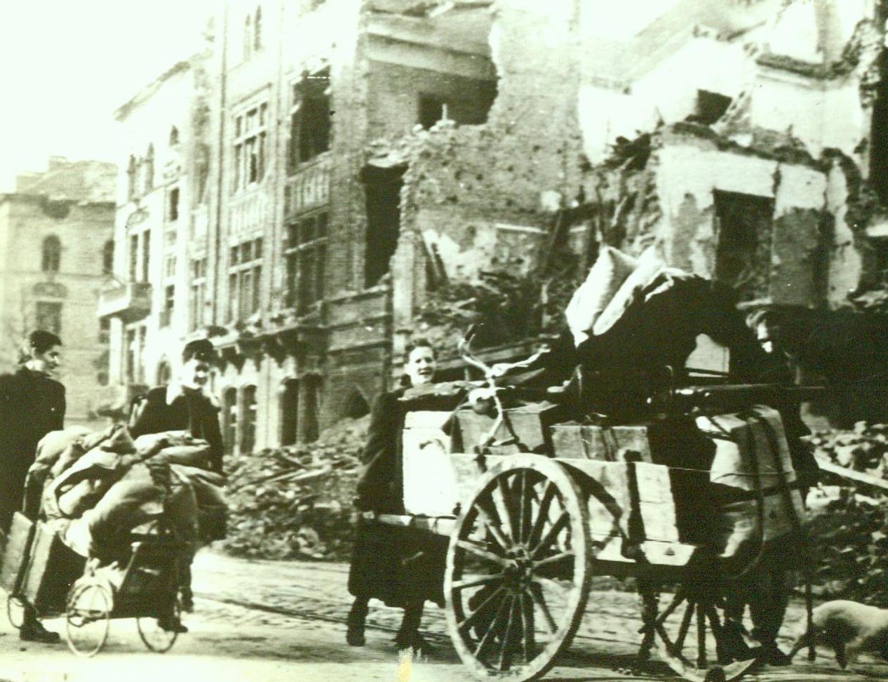 Refugees Flee Aachen, 10/16/1944. Aachen, German – Pushing carts piled high with their few salvaged belongings, German women flee doomed Aachen. The refugees pass through a ruined street, walking past shell and bomb-torn buildings. 10/16/44 (ACME);
