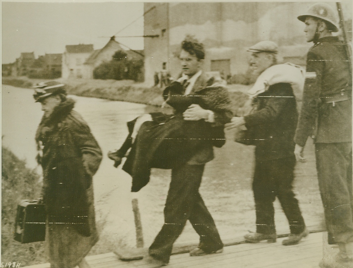 Spared By Truce, 10/1/1944. Calais, France—Given the chance to leave embattled Calais during a 24-hour truce between the attacking Allies and the defending Nazis, civilians cross a bridge spanning Calais Canal as they hurry out of the port city. One old woman, too weak to walk, is carried away by a neighbor. Shortly after the truce ended, Canadian troops were in possession of the bomb-torn seaport.  Credit: Army radiotelephoto from ACME;