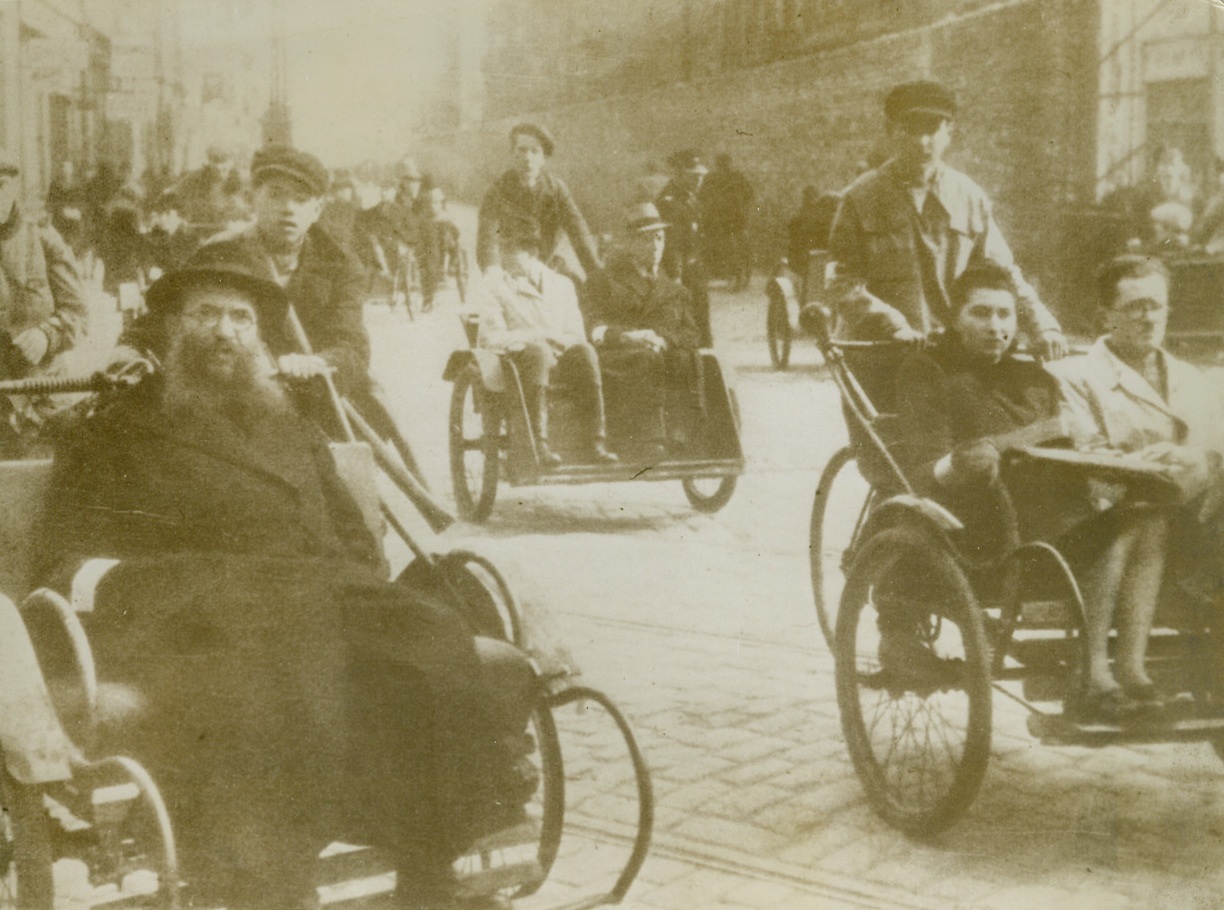 NO “CABS” IN A GHETTO, 2/1/1944. OCCUPIED EUROPE—Young Jewish boys push home-made “taxis” through the street of a ghetto in German occupied Europe. Guarded on the outside by the Gestapo, and on the inside by Jewish police, the inhabitants of the ghetto are segregated from the rest of the country. Received through a neutral source, this is one of the first photos to show a typical day-by-day existence in a Nazi-created ghetto.Credit: Acme;