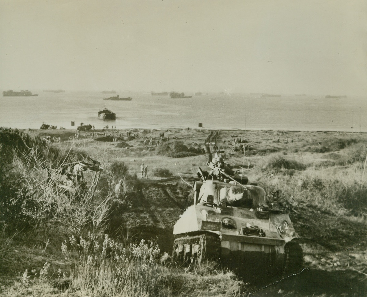 On the Road to Rome, 2/3/1944. Italy—An American tank rolls up a hill from the invasion beach, where it was landed during the first stages of the Allied capture of beachheads in the Nettuno-Anzio area in the drive on Rome, last Jan. 22. Standing off the beach (background in photo) can be seen some of the ships of the huge Allied invasion fleet (passed by censors). Credit: ACME.;