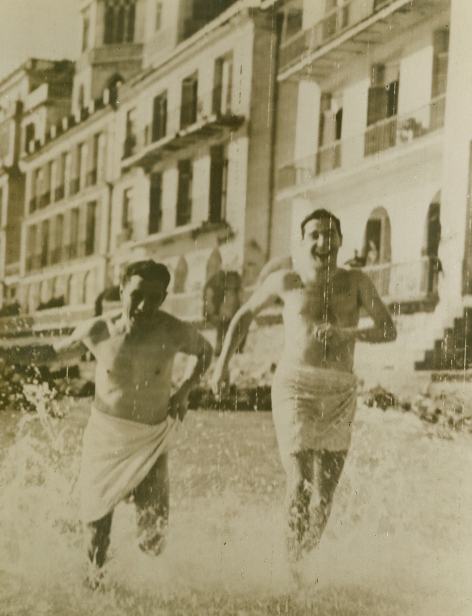 Yanks in “Surf Blitz”, 2/2/1944. Nettuno, Italy—Cpl. John Chiodo, (left), of Johnston, PA., and Pvt. Murrell Winner, of Louisville, KY, take time out for a dip in the surf at the once-famous bathing resort of Nettuno—one of the Allies’ beachheads in their drive on Rome. Today, the British and Americans have reached Campoleone and are only 15 miles from the Eternal City. Note beautiful villas in background (photo above). Credit: ACME photo by Bert Brandt for the War Picture Pool via Army radiotelephoto.;