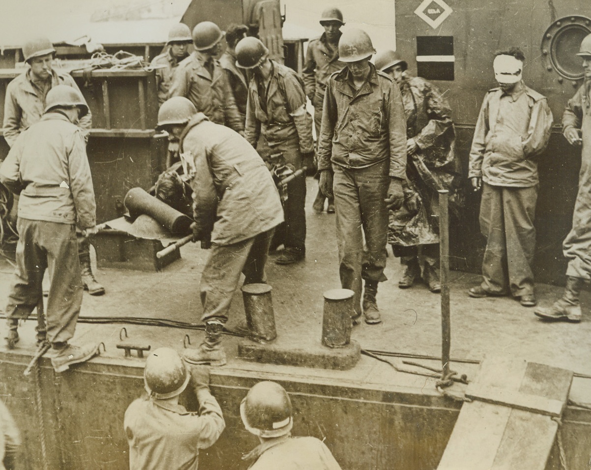 Battered at Beachhead, 2/11/1944. ITALY – Injured fighters who are able to walk, watch their more seriously wounded comrades being loaded aboard a warship off the Anzio-Nettuno beachhead. The shore may be seen, dimly, in the background.Credit Line (ACME);