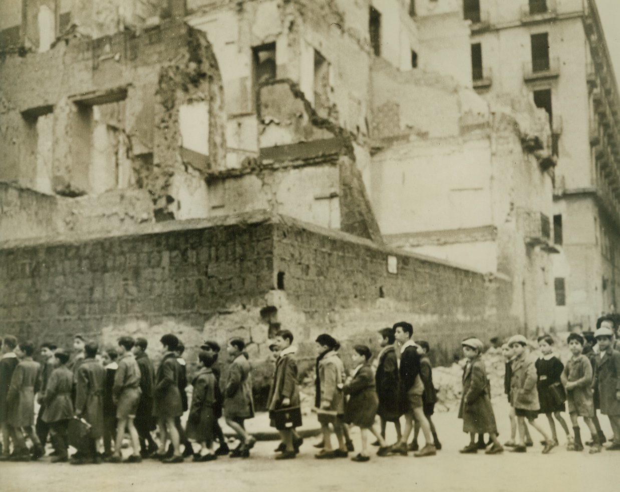 Vacation Over for Naples Kids, 2/14/1944. NAPLES, ITALY – Naples children, who have had a long holiday from the classroom as they hid from both Allied and Nazi bombs, now file back to school, passing war ruins on the way. Many Neapolitan families moved into hillside caves as war rocked their city. Credit Line (Acme);