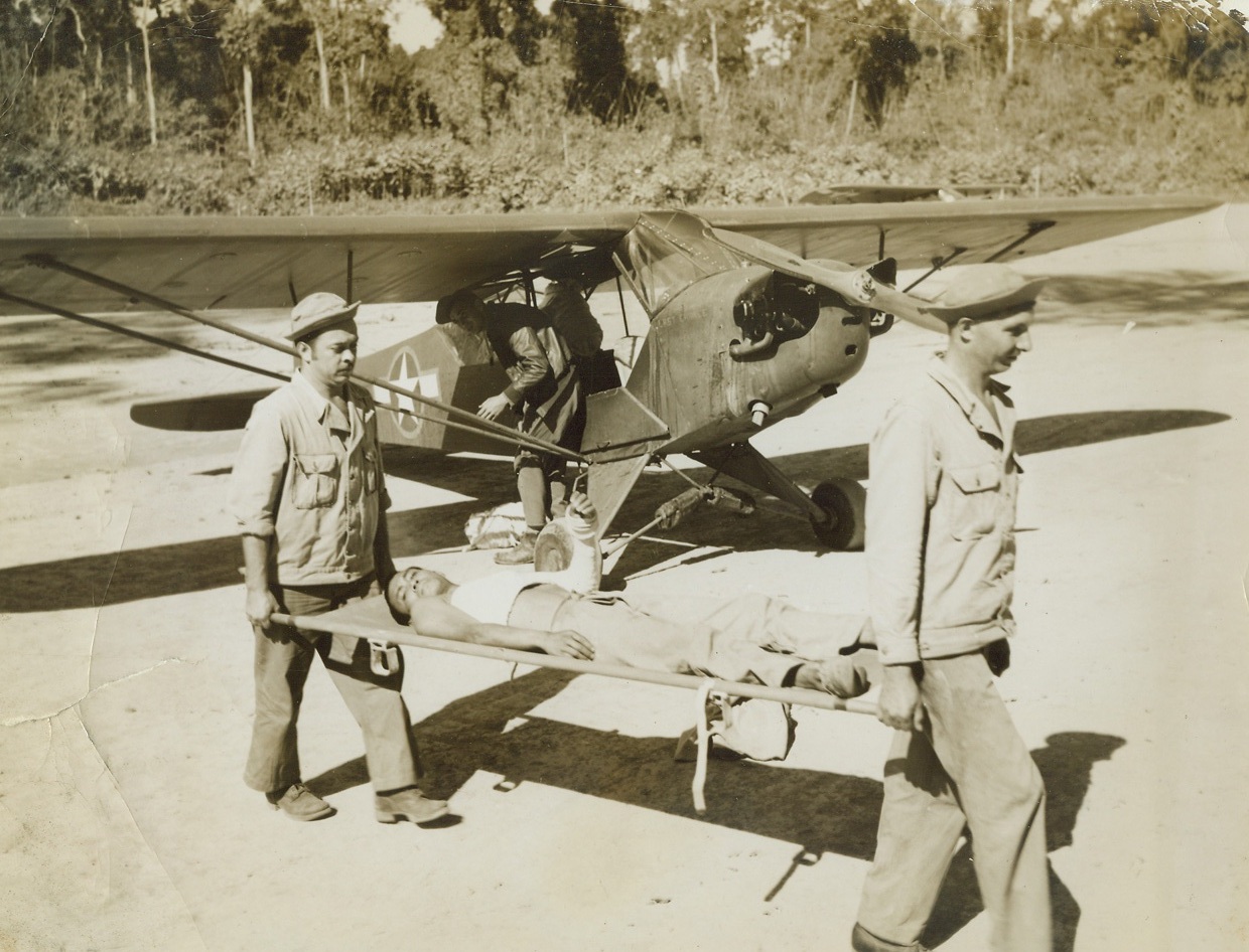 Winged Midgets of the Jungle, 2/3/1944. CBI War Theater – While American bombers and fighters roar into the headlines, a vastly different type of U.S. Army “Air Force” works quietly and efficiently on its own, hidden war fronts. Small and rugged Cubs and Sentinels, piloted by enlisted men who built up their flying time in civilian life, are skimming the jungles, hopping over mountain ridges, and soaring through ragged canyons, on missions invaluable to American, British, and Chinese troops in the CBI War Theater. No guns are carried by the Midget Aircraft. The main “weapon” of the Cub or Sentinel is maneuverability, and when charged by the enemy, the tiny plane adopts the tactics of a mosquito evading a hawk. A Chinese soldier, wounded in Burma, is brought back to a base hospital by a Sentinel (background). Other mercy missions of the Midget Plane include the dropping of food and medical supplies to frontline jungle warriors. Credit: ACME photo by Frank Cancellare, War Pool Correspondent;