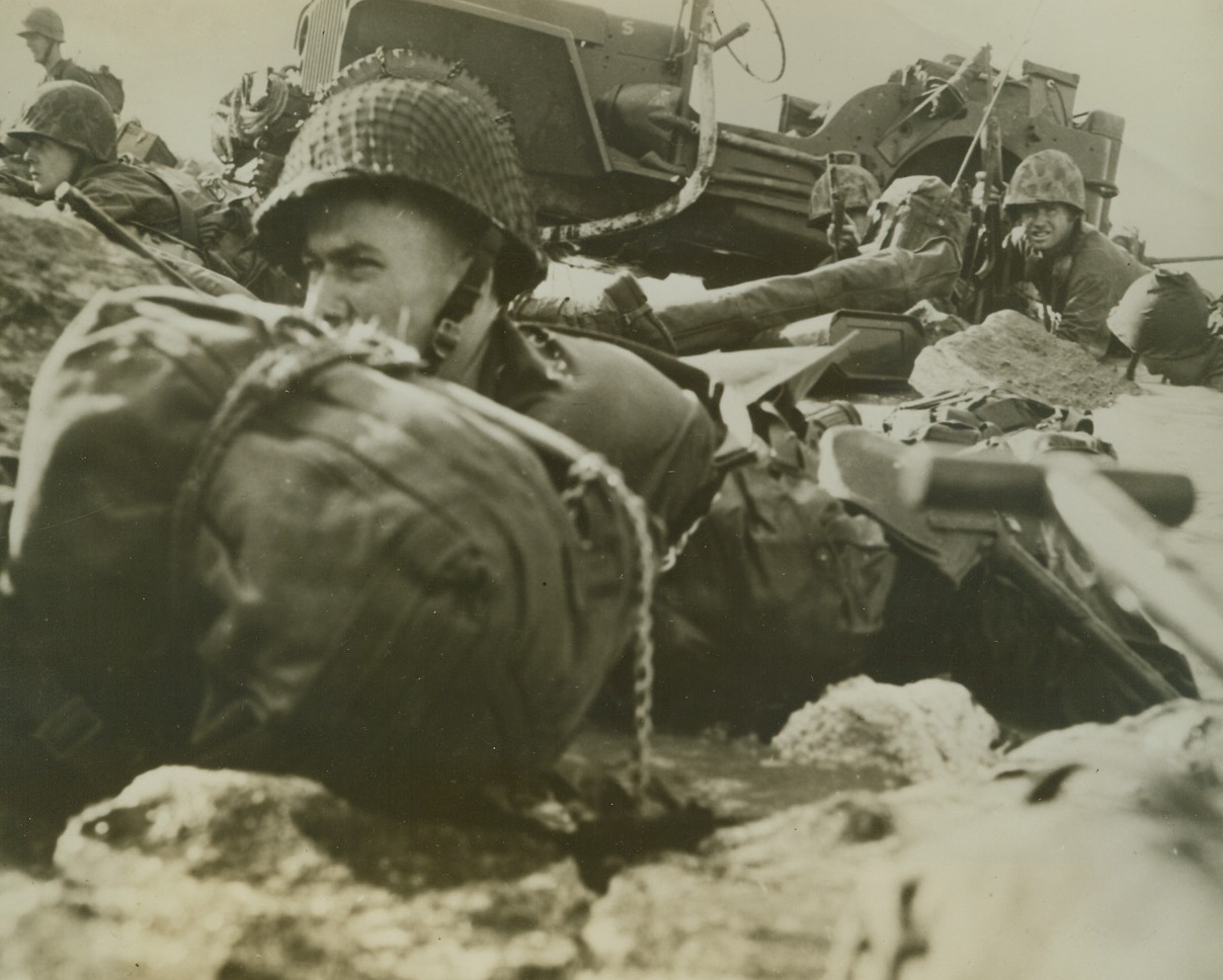 Marines Hit the Beach at Eniwetok, 2/25/1944. Eniwetok Island – Marines crouch in surf on beach of Eniwetok Island, waiting for naval and air bombardment to lift before they storm Jap positions on island.Credit Line (ACME);