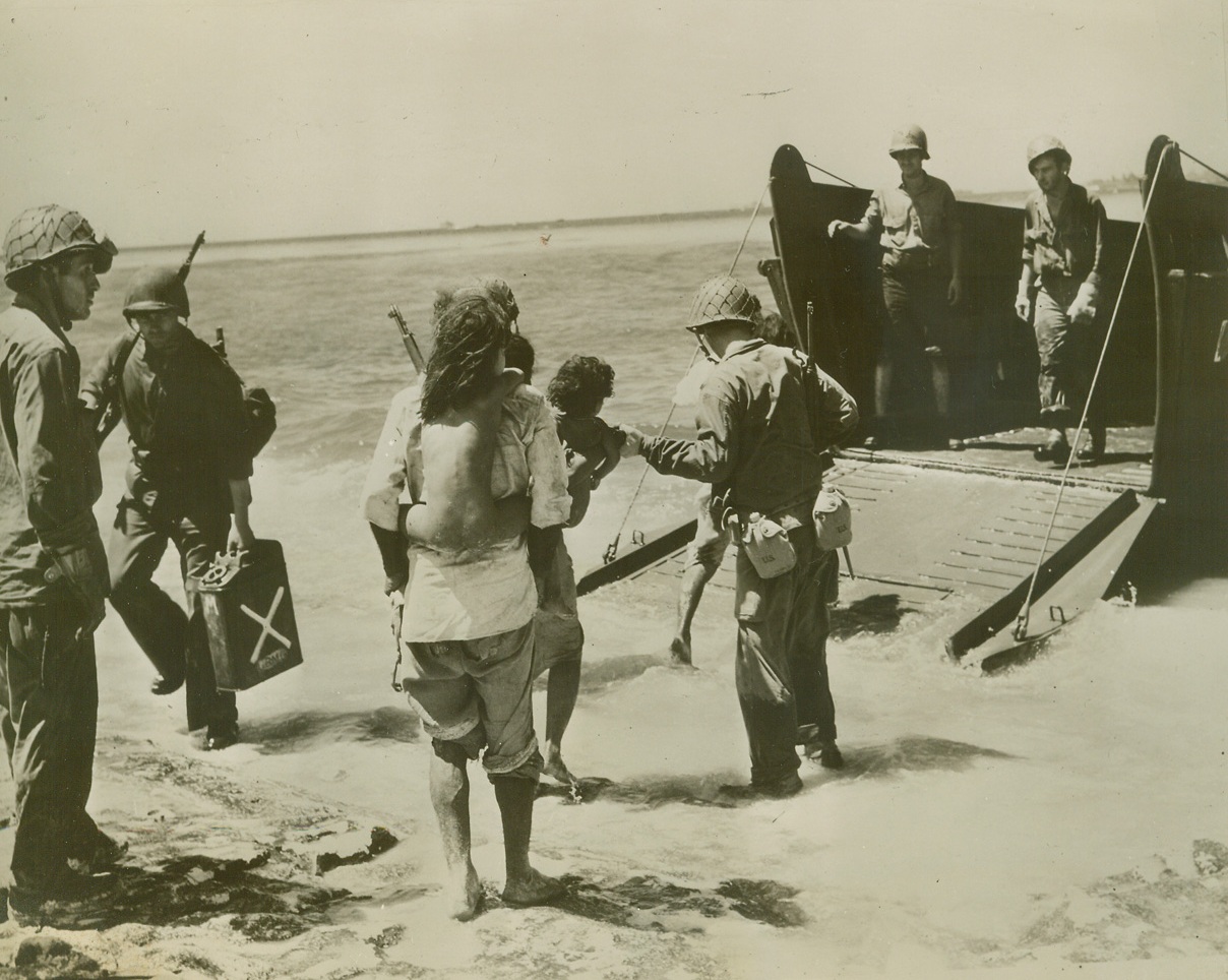 Moving Day for Natives, 2/9/1944. ENIWETOK - While the battle rages for islands of the Eniwetok Atoll in the Marshalls, this family of natives is removed from the danger area in a Coast Guard manned landing craft, which a few moments before had landed assault troops on the island. In foreground, the native father carries his nude daughter pig-a-back, while, in front of him, mother totes a tiny son in her arms.;