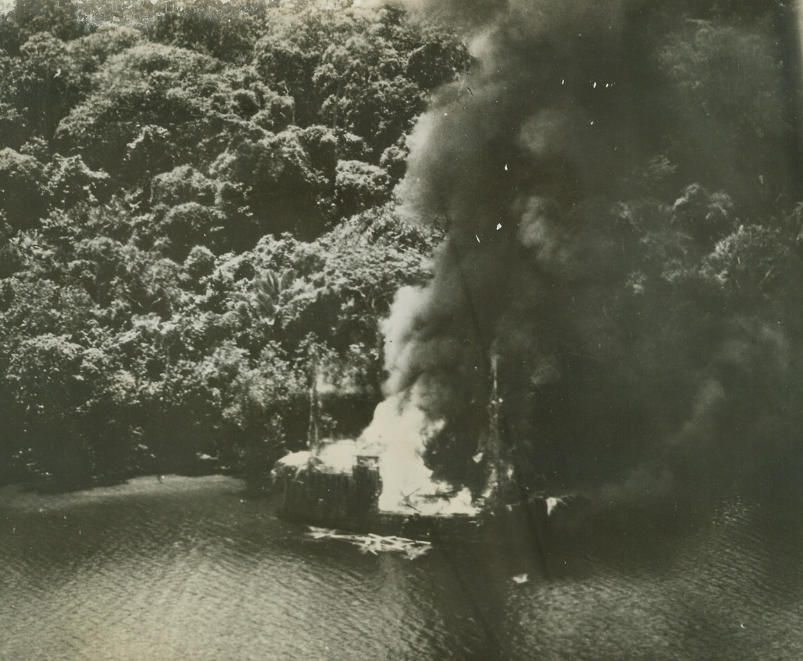 Nip Truck Nipped, 2/24/1944. New Guinea – This Jap barge attempted to sneak down the North coast of New Guinea, covered with camouflage and moving close to overhanging trees ashore, but Australian Beaufighters spotted the ship and blastd it.  Here, it is aflame from stem to stern after bombs of the Royal Australian Air Force had caught her.Credit Line (R.A.A.F. photo via U.S. Army Air Forces from ACME);