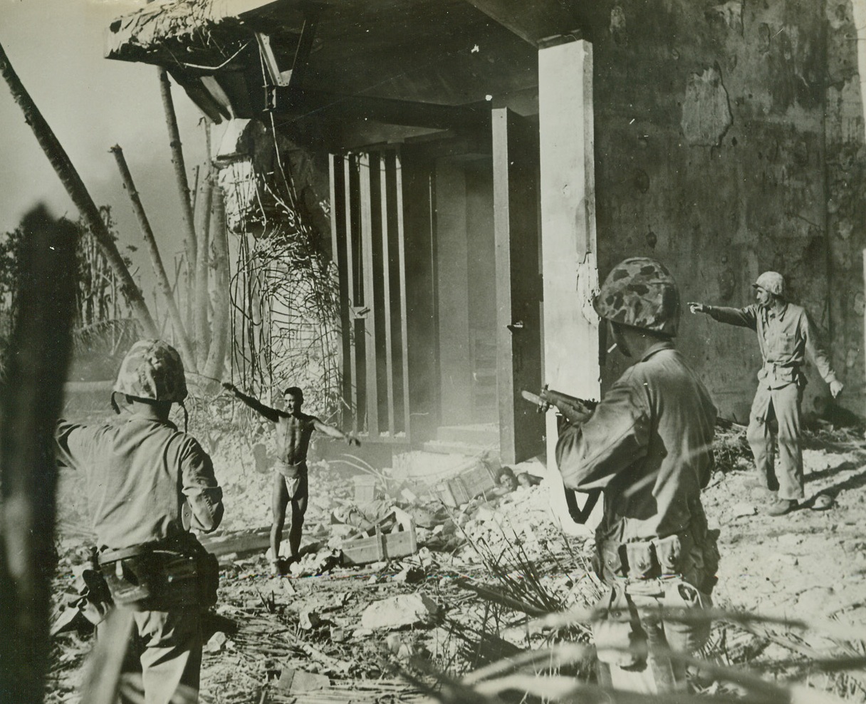 Bursts blockhouse Reveals 20 Japs, 2/16/1944. Namur Island – Thirty-six hours after Namur Island on Kwajalein Atoll in the Marshalls was “secured”, a supposedly silenced Jap block house blew up, bursting a steel door.  A Jap soldier stumbled through and three more were found inside.  There had been 20 Japs in the block house before the explosion.  Here suspicious Marines direct an uninjured Jap, clad only in a loin cloth, away from the building, as another crawls out from wreckage beneath the door.  A third Jap lies dead between them. Credit (U.S. Marine Corps photo from ACME);