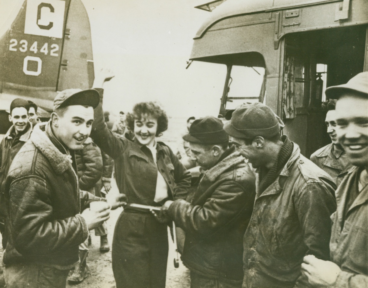 Clubmobile Gals, 2/19/1944. Somewhere in England—Based at a large, 15th century mansion owned by an English Earl and his Countess, four American Red Cross girls staff a Clubmobile bus, one of 51 such mobile canteens operating in the British Isles. Katharine Spaatz, 22-year old daughter of Lt. Gen. Carl Spaatz, is one of them. Pounding their “beat” of several camps and airfields within easy riding distance of their base every week, the girls hand out doughnuts and coffee and generally serve as morale boosters for their G.I. customers. This series shows the quartette at their jobs. New York Bureau “She’s a perfect 42, fellas,” this mechanic teases Dorothy Myrick as the boys measure her waist at a Flying Fortress repair depot. The Red Cross girls come in for a lot of good-natured kidding from the servicemen, with whom they become quite friendly. Credit: ACME.;