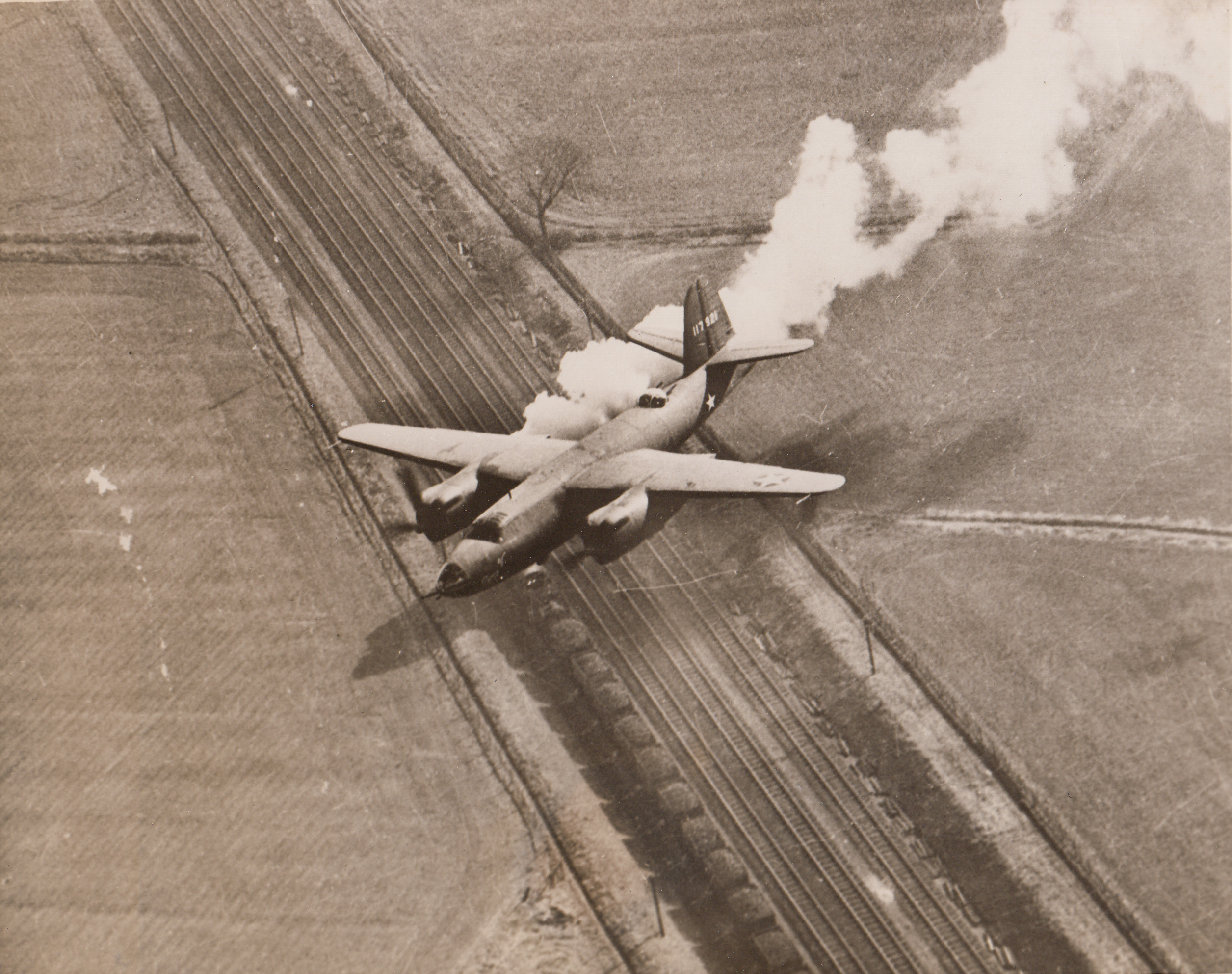 FOOLED YOU, DIDN'T IT?, 2/16/1944. ENGLAND—At first glance it would seem that this B-26 Marauder is coming home in distress with its right engine ablaze. Actually the white smoke is puffing from a locomotive on the tracks below. A fast-thinking aerial photographer in another Marauder snapped the optical illusion returning from a raid over occupied Europe.;
