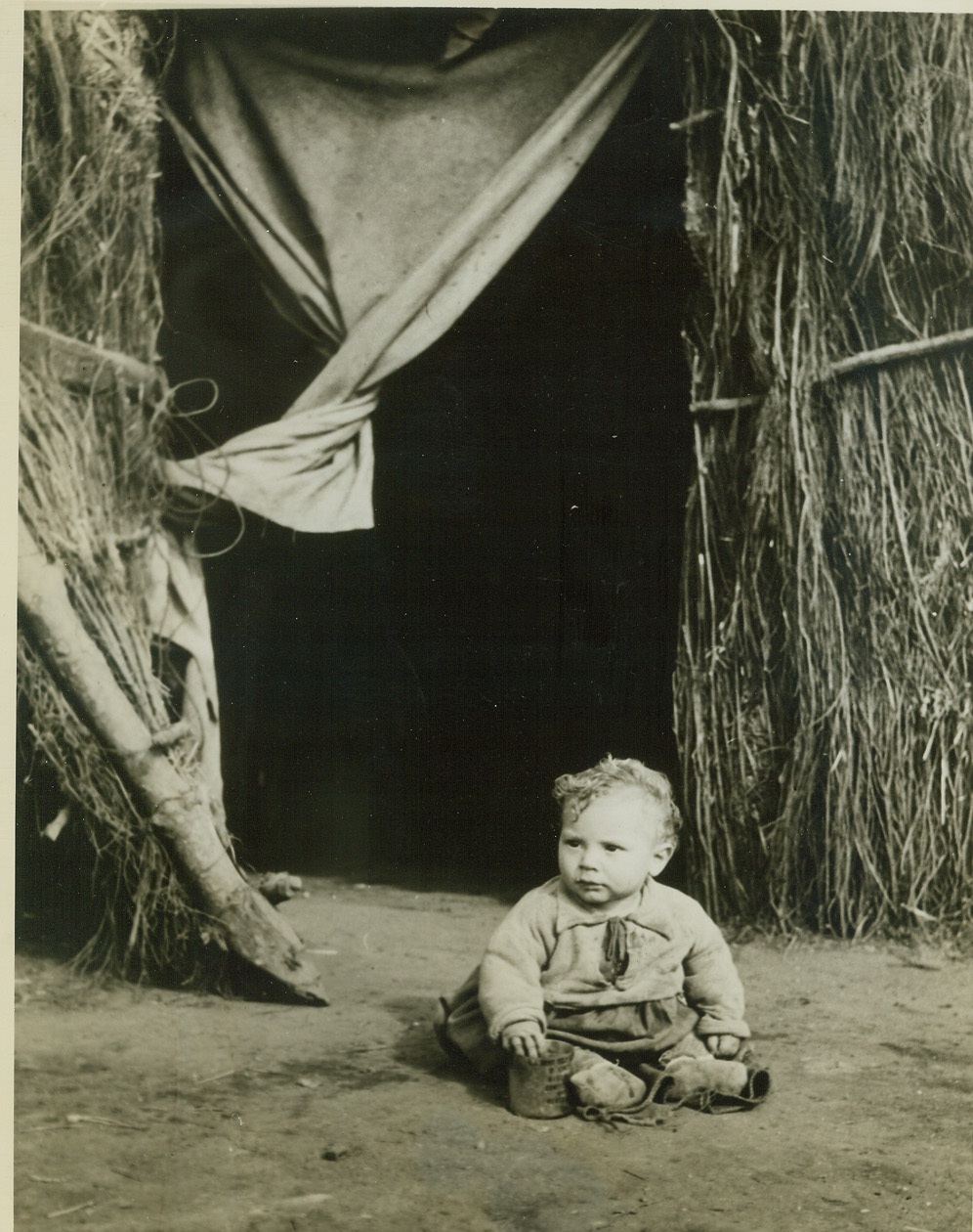 Grass Hut is Home to Him, 3/4/1944. Anzio, Italy – Playing quietly outside the entrance to the uncomfortable grass hut in which he and his folks live, this very young Italian boy is a member of one of many families left homeless when war came to Anzio. Their original home completely destroyed in the beachhead battle, the child’s family found refuge in the hut. Credit: (Official U.S. Navy Photo from ACME);