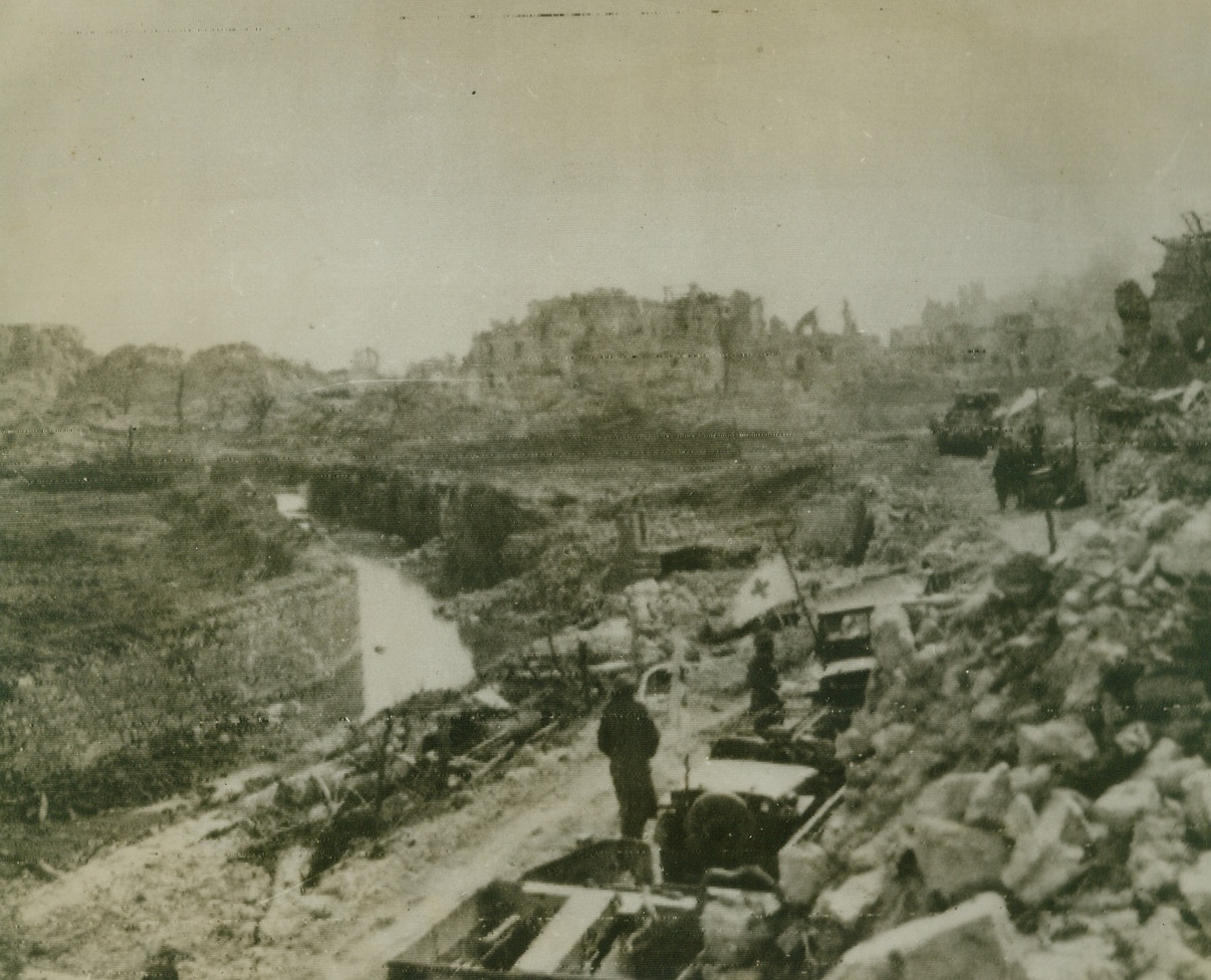ENTERING “CITY OF THE DEAD, 3/20/1944. This photo, flashed to the U.S. by radio today, shows a long line of Red Cross and patrol vehicles, pausing behind the shelter of piles of rubble, just before entering Cassino, Italy, following the Allied “obliteration raid”—heaviest of the war—on the town. German paratroops, landed after the raid, put up stubborn resistance, but today, all but a section of the southern part of Cassino was in Allied hands. Note ruined buildings (background in photo) marking the terrific destruction wreaked by Allied bombs.Credit: U.S. Signal Corps radiophoto from Acme;