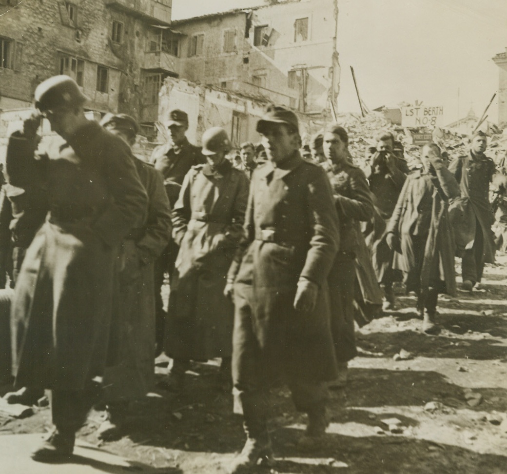WOULD-BE CONQUERORS REACH ANZIO, AT LAST, 3/4/1944. ANZIO, ITALY—Anzio was the goal for these Nazi warriors, who fondly hoped to march through the Italian town as conquerors. But they came to Anzio as prisoners, taken in the bloody battle for the beachhead below Rome. Some try to hide their faces as they march down to a ship that will take them to a behind-the-lines prison camp. In background are the ruins of the Italian coastal town. Credit: Official U.S. Navy photo from Acme;