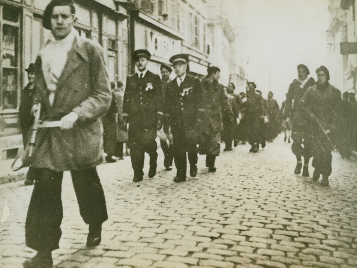 Maquis Take Over, 3/28/1944. OYONNAX -- November 11, 1943 will be long remembered by natives of Oyonnax, 20 miles west of Geneva, for that was the day on which the Maquis took over the town for a two-hour Armistice Day celebration. Demonstrating their ability as soldiers, the Maquis "captured" the town, held the celebration, and drove back to their hidden camps. Meanwhile Nazi and Vichy authorities waited 12 miles away, deceived by posters announcing that the celebration would be held in another town. Here the Maquis march thru the streets of Oyonnax, with French Air Force officers in foreground. Credit Line (ACME);