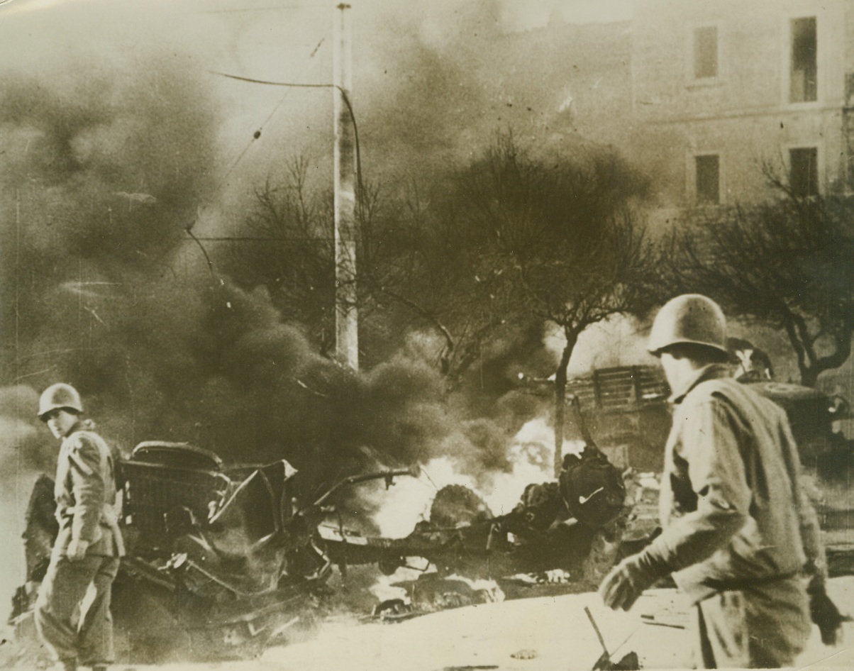 After the Raid, 3/11/1944. NETTUNO, ITALY – Two Yanks examine the still-flaming remains of Army vehicles that were set on fire by bombs during a German air raid on Nettuno. The raiders visit the beachhead areas so regularly that the Allied Military Government has moved the entire civilian population of Nettuno and neighboring Anzio to less dangerous areas.Credit Line – WP – (Acme);