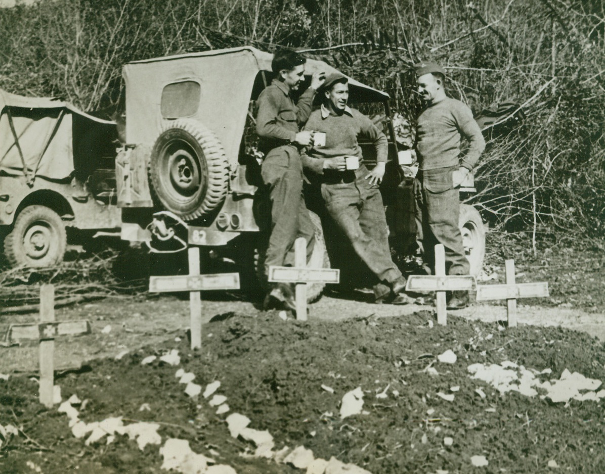 Over the Coffee Cups, 3/20/1944. ITALY – Leaning against a Jeep, Allies from Texas and New Zealand, enjoy a cup of coffee “somewhere in Italy.” Left to right, are: Pvt. Howell Hasten, Lorreta, Texas; and Gunner Ted Boys, of Hellersville, N.Z.; and Gunner Jim Jenkins, of Christ Church, N.Z. In the foreground are German graves left by the enemy in his retreat toward Cassino.Credit Line (Acme) (WP);