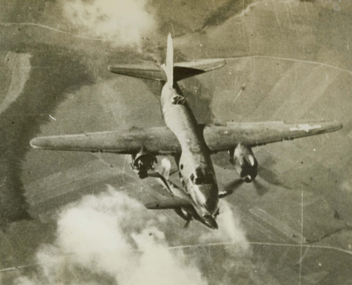 One Engine Still Going Strong, 3/9/1944. OCCUPIED EUROPE – A direct hit from a Nazi flak battery tore out an entire engine (left of photo) of this Ninth Air Force Marauder just a few seconds before the aerial photo was made from another bomber in the formation. The crippled B-26 medium bomber is shown falling behind in the formation. Below, another Marauder flies on, untouched by the heavy curtain of flak.Credit Line (Acme);