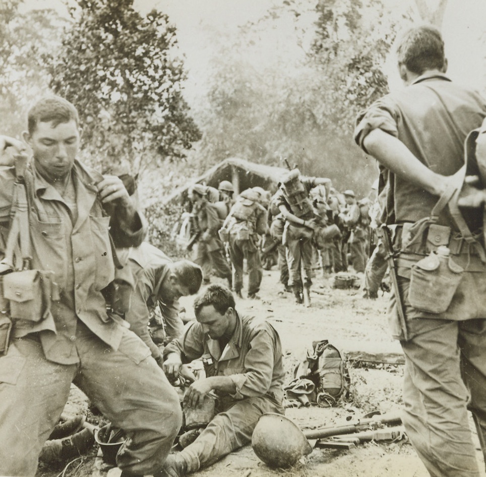 A Brief Rest for the Weary, 3/31/1944. Northern Burma – Battle-weary Yanks rest during a brief meal period in a deserted Kachin Village in the Hukawng Valley, Northern Burma. The troops have just returned from four days continuous fighting in the front lines. They are members of Gen. “Joe” Stilwell’s American and U.S. trained Chinese forces, who are successfully driving out the Japs from Northern Burma. Credit: ACME;