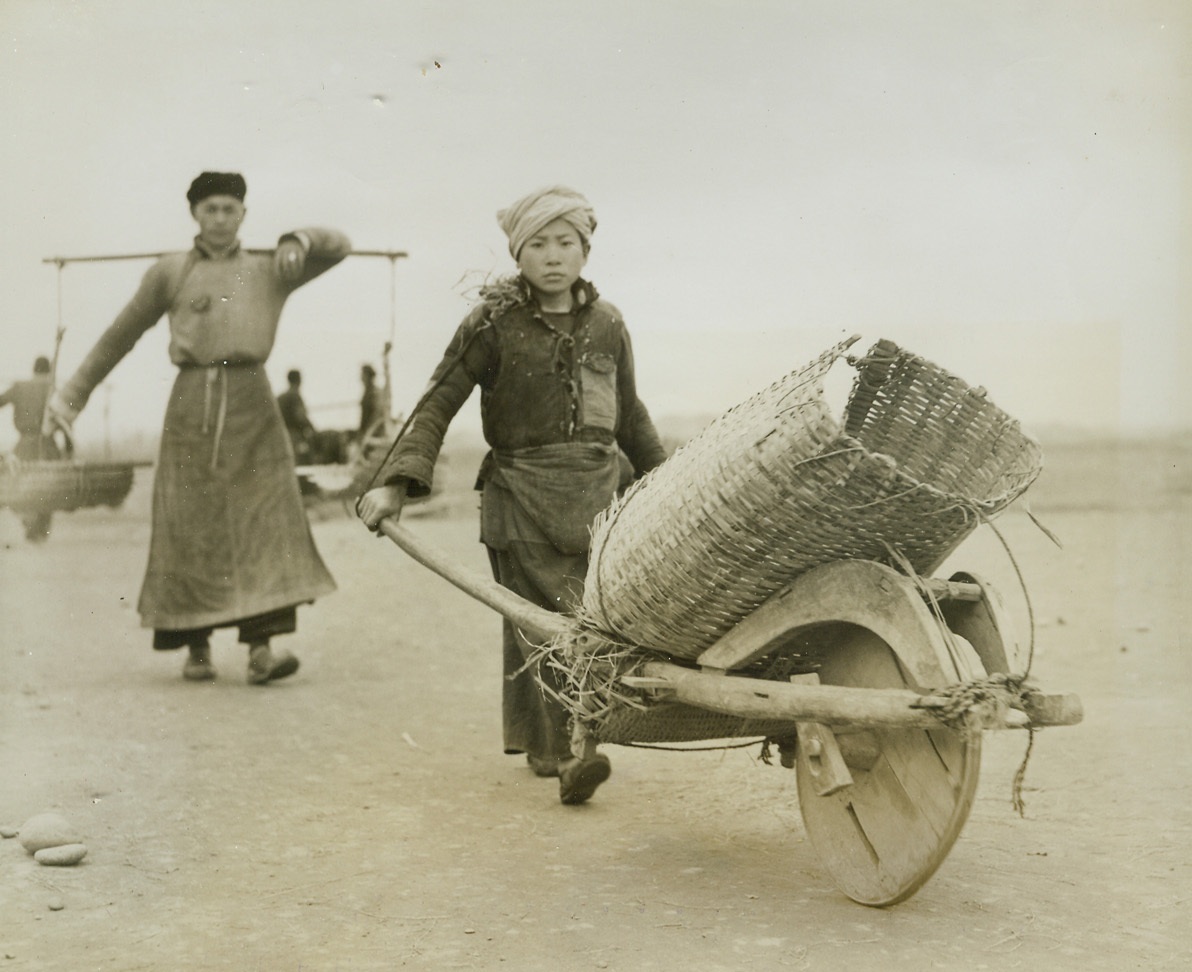 Airfield—Handmade, 3/31/1944. Lack of modern equipment and machinery isn’t stopping the resourceful from building modern airfields in China. Three hundred thousand Chinese workers have been conscripted to do the job. A hundred thousand little handmade wheelbarrows are used to transport materials—and even the chipping of stones for the runways is done by hand. American engineers working in conjunction with expert Chinese army engineers are supervising the job. Photo shows: a young Chinese boy carries essential materials to a runway, using a wheelbarrow constructed of bamboo and wood to carry his load.Credit: ACME Photo by Frank Cancellare for the war picture pool.;