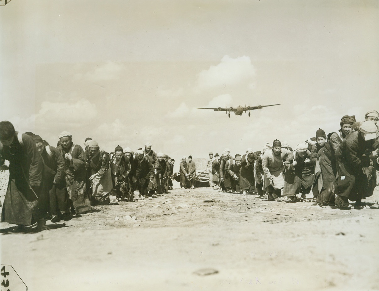 Airfield -- Handmade, 3/31/1944. China – Lack of modern equipment and machinery isn’t stopping the resourceful Chinese from building modern airfields in China.  Three hundred thousand Chinese workers have been conscripted to do the job.  A hundred thousand little handmade wheelbarrows are used to transport materials – and even the chipping of stones for the runways is done by hand.  American engineers, working in conjunction with expert Chinese Army Engineers, are supervising the job.  Photo shows: drawing a sharp contrast between modern machinery and medieval labor, this Liberator boars over a group of coolies as they strain at the back-breaking job of hauling a huge stone roller over the runway. Credit line(ACME photo by Frank Cancellare for the War Picture Pool) – WP;