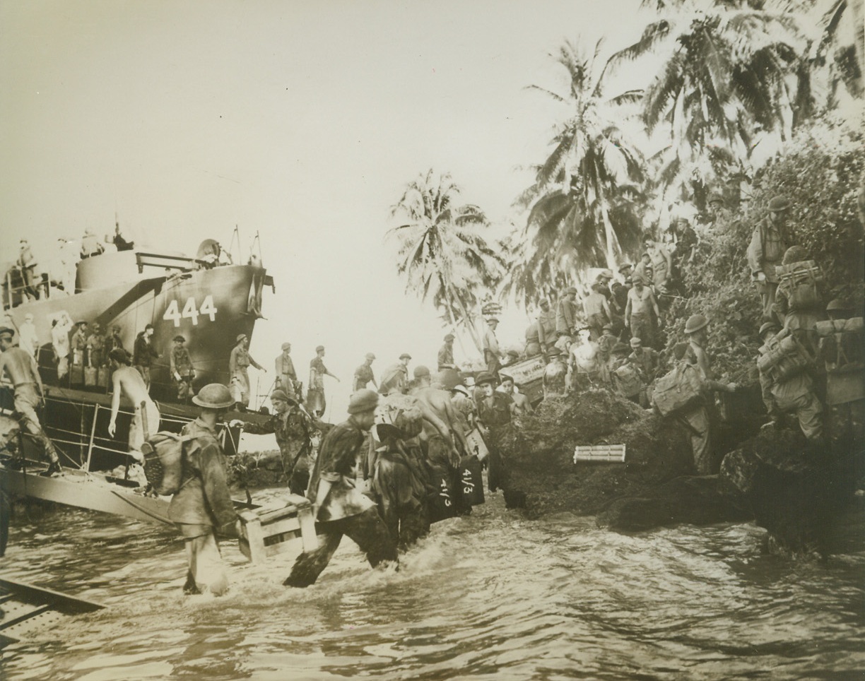 Green Islands in Allied Hands, 3/13/1944. Washington, D.C:  American and New Zealand forces, covered by the U.S. Navy, land and occupy the Green Islands just North of Bougainville.  This photo, made a right after the landing, is typical of others in the growing list of Pacific invasions.  Overhanging palms and thick underbrush border the shore where sweating New Zealanders, rifles set aside for the time, labor in the tropic heat to unload a landing craft. Credit (ACME);