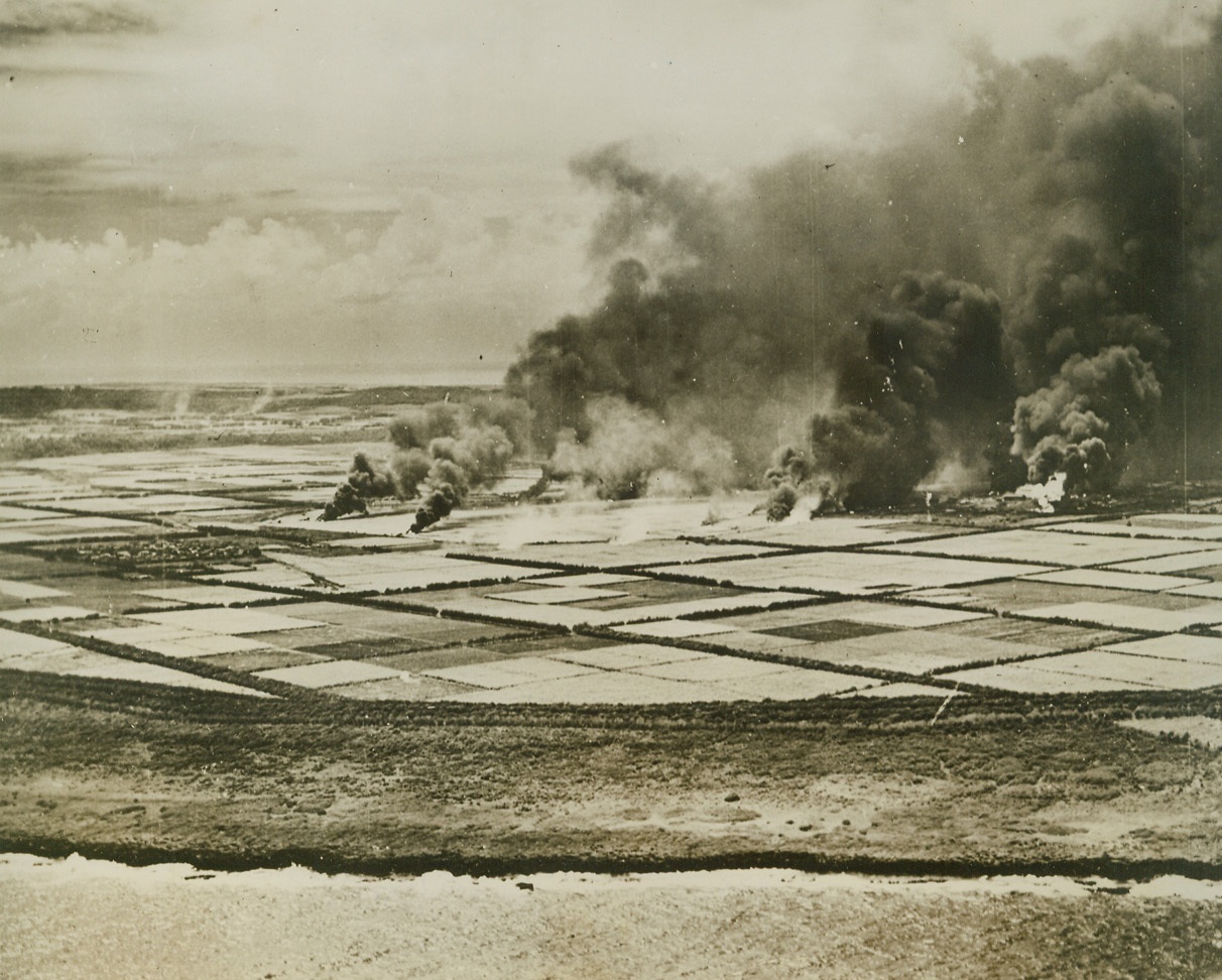 Tinian Island Airstrip Bombed, 3/6/1944. Tinian Island – Japanese planes burning on airstrip on Tinian island, Jap stronghold in the Mariannas, following attack by U.S. Navy carrier-based planes on Feb. 23rd.  Sugar cane fields form a pattern around the airport.Credit line (U.S. Navy photo from ACME);