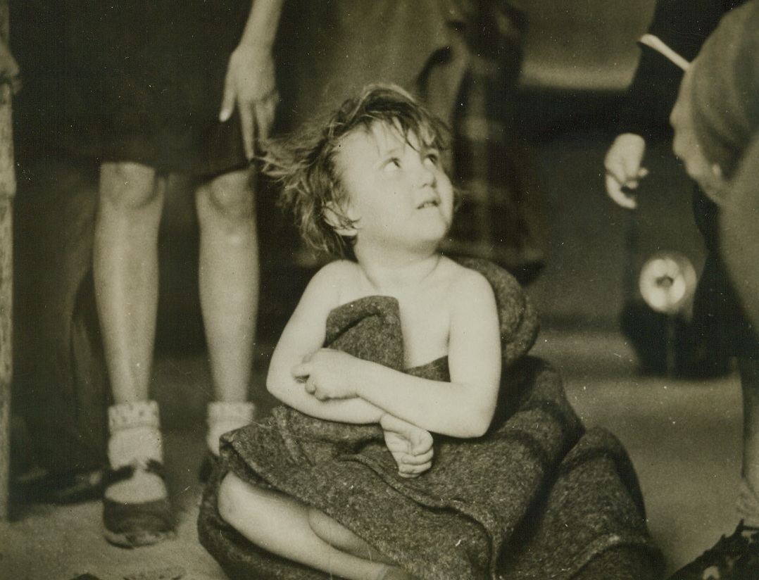 Hiding Her Shame, 3/11/1944. Middle East—Hugging a blanket to her nakedness, this embarrassed little Yugoslav refugee exchanged her rags for American Red Cross clothing when she arrived at a desert camp in the Middle East with a contingent of 25,000 Yugoslav partisan refugees. Aided in their escape from the Adriatic coast and islands by underground elements of Marshal Tito’s guerillas, women and children in the group were accompanied by only aged and disabled men. They will be resettled in the Middle East by British authorities. This is an exclusive ACME photo.Credit: ACME.;